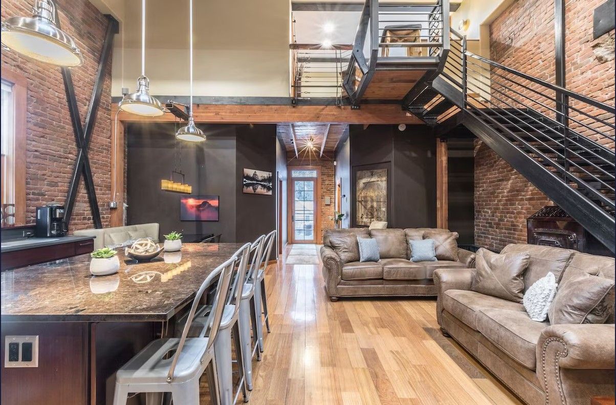 The inside of a modern loft Airbnb rental in Ouray showing the metal staircase, granite kitchen island, and leather couches.