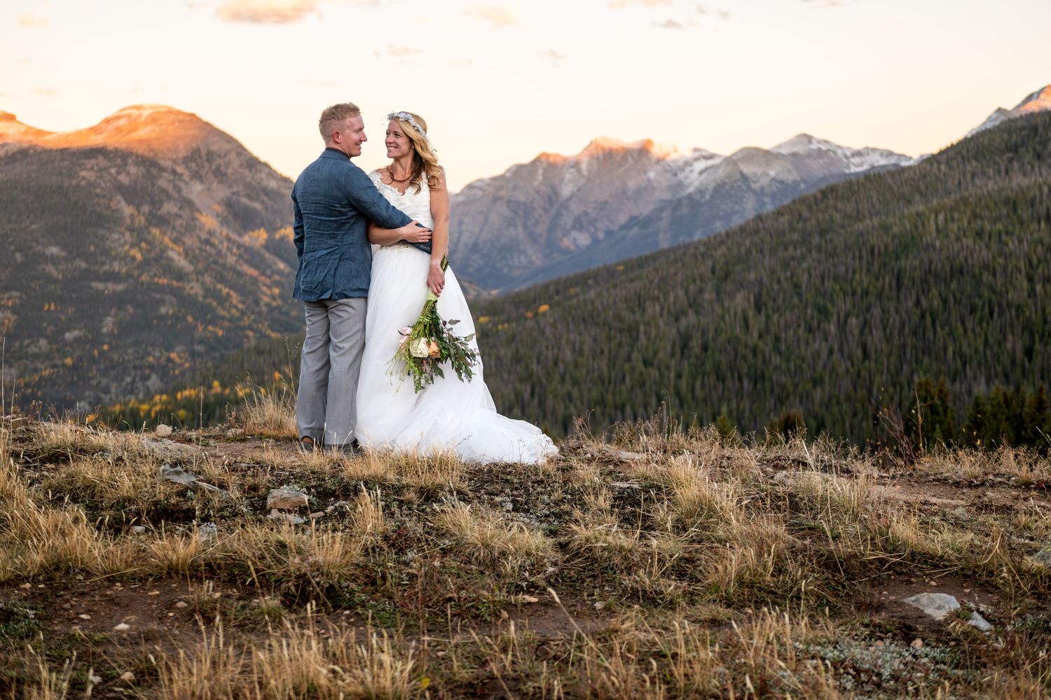 An eloping couple embraces against stunning mountain backdrop during sunset in the San Juan Mountains. Fall colors can be seen behind them.