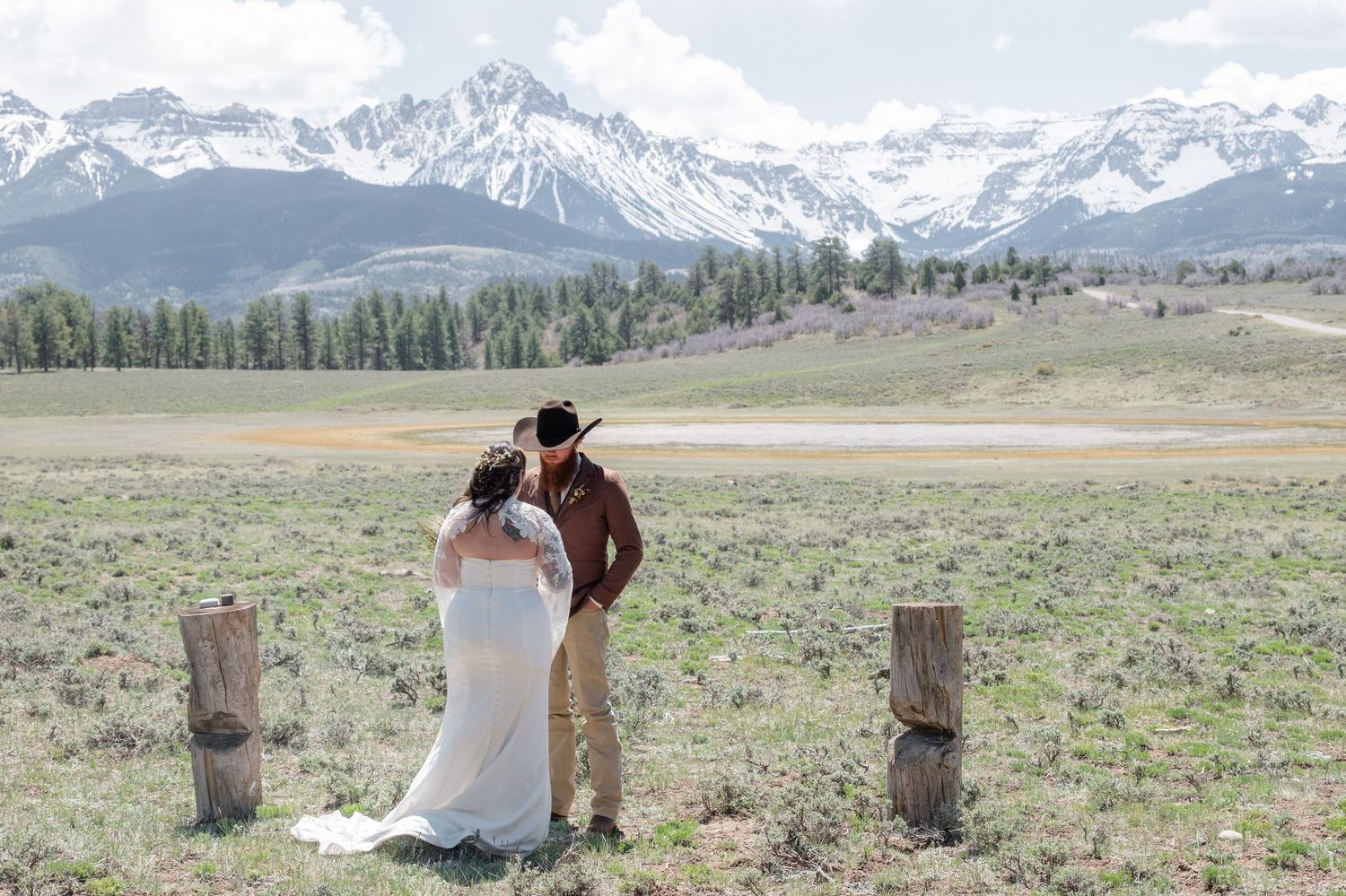 Bride and groom share a romantic moment in a scenic mountain meadow with snow-capped peaks in the background.