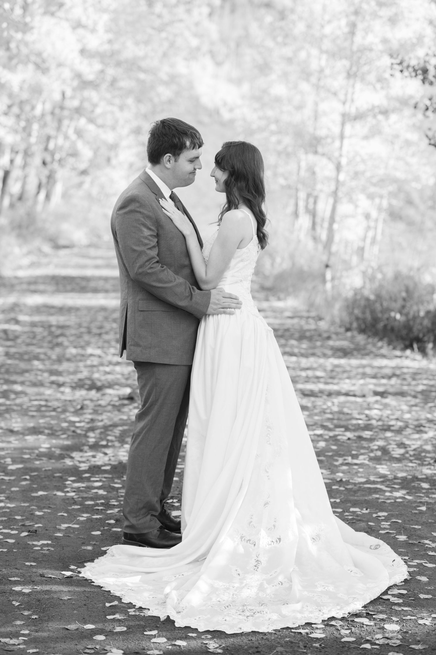 Black and white photo of a bride and groom embracing outdoors, surrounded by autumn leaves and trees.