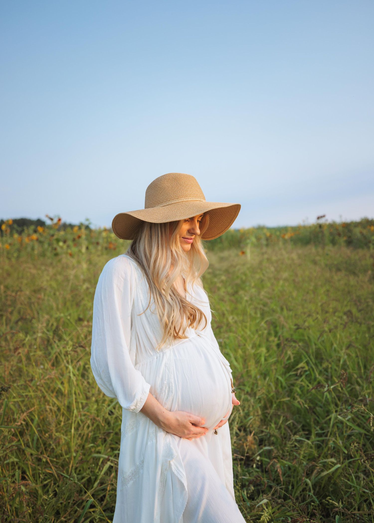 Pregnant woman in a field with her hands under her baby bump, surrounded by tall grass during golden hour in Snohomish, photo by Tim Neal.