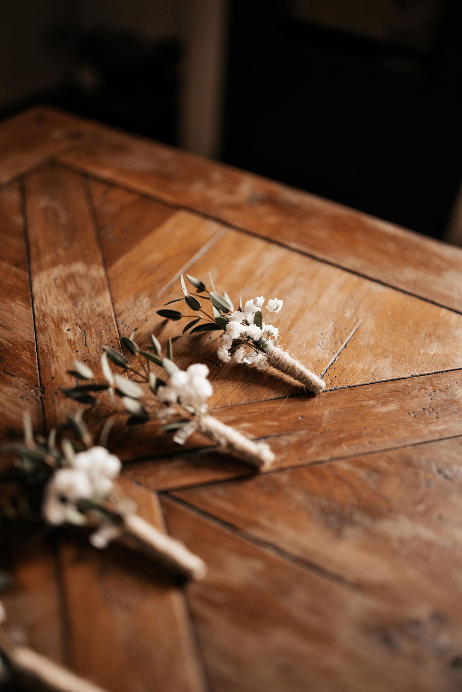 Des boutonnières de mariage avec de délicates fleurs blanches et de la verdure reposent sur une surface en bois rustique.