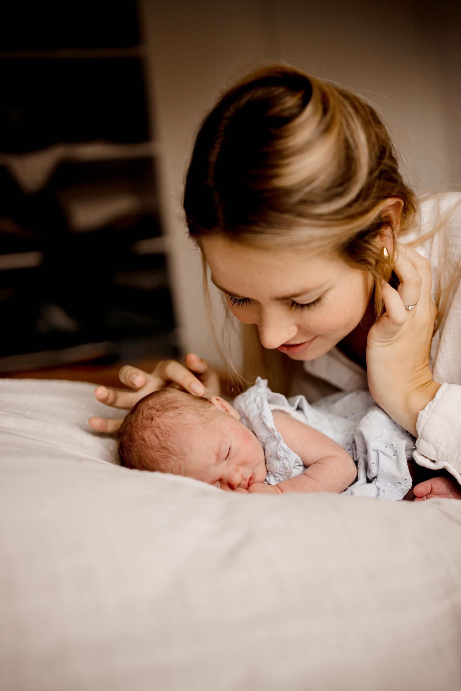 Tender moment with sleeping newborn on white bedding.