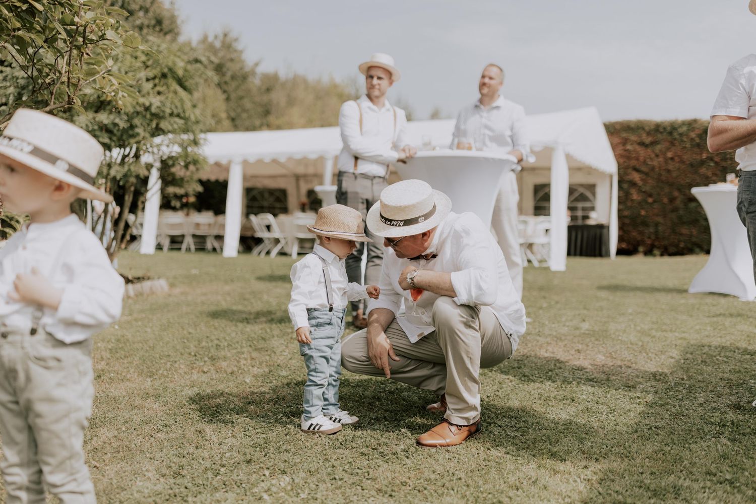 Rassemblement extérieur sur le thème du blanc avec des parents et des tout-petits interagissant sur une pelouse ensoleillée.