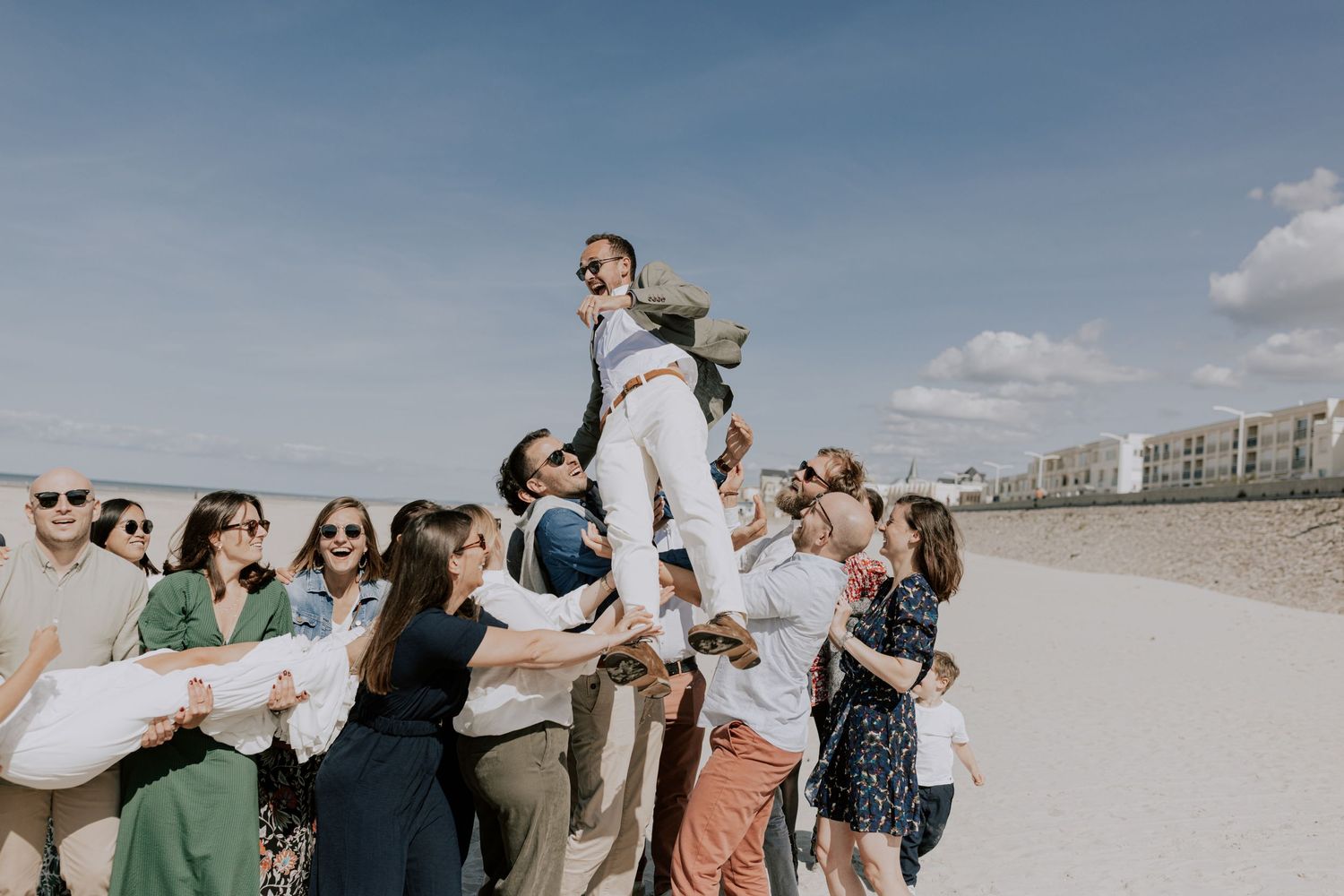 Un groupe d'amis soulèvent le marié lors d'un mariage en plein air sur la plage.