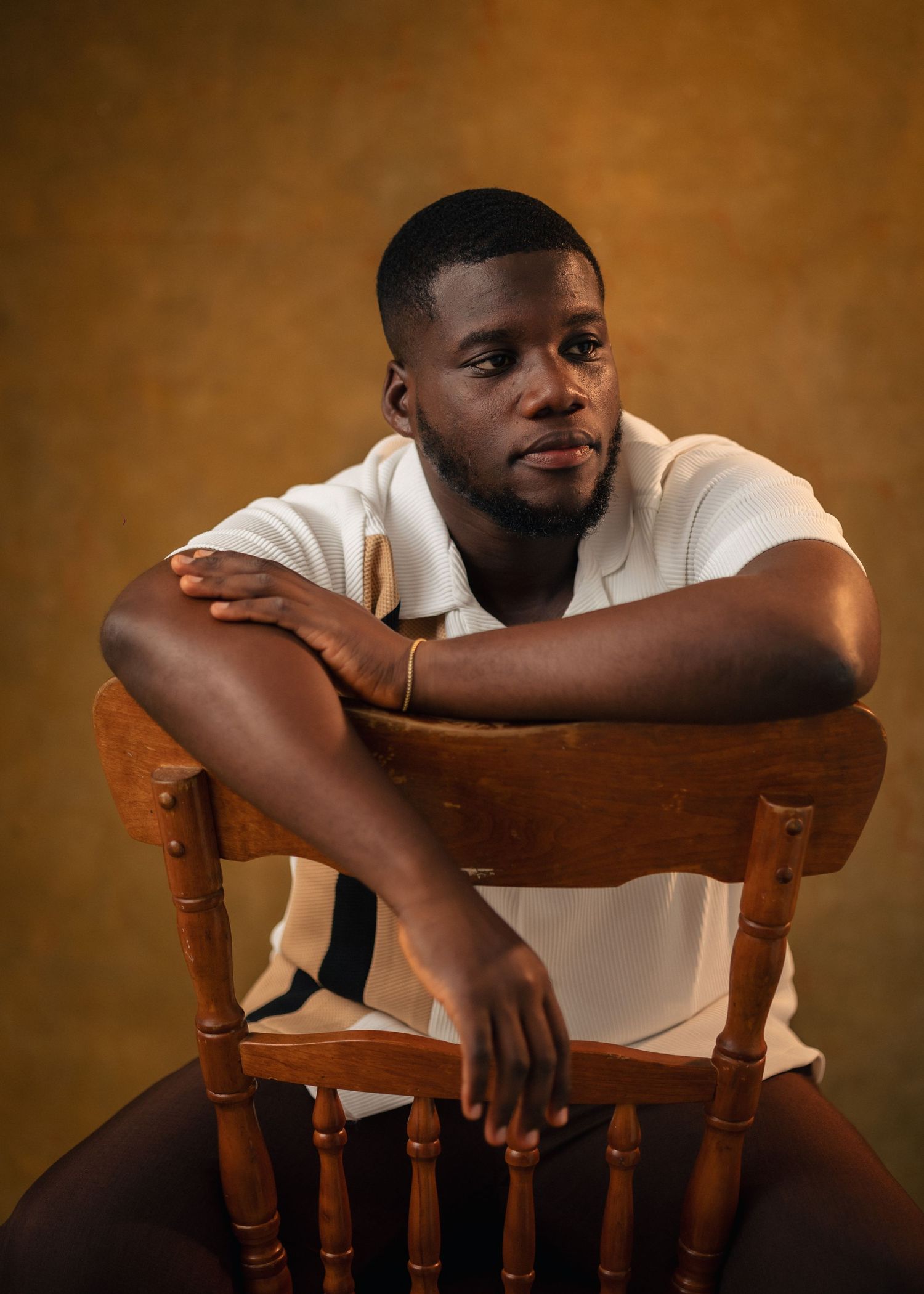 A series of portraits showing someone in a white shirt leaning thoughtfully on a wooden chair against a brown backdrop.