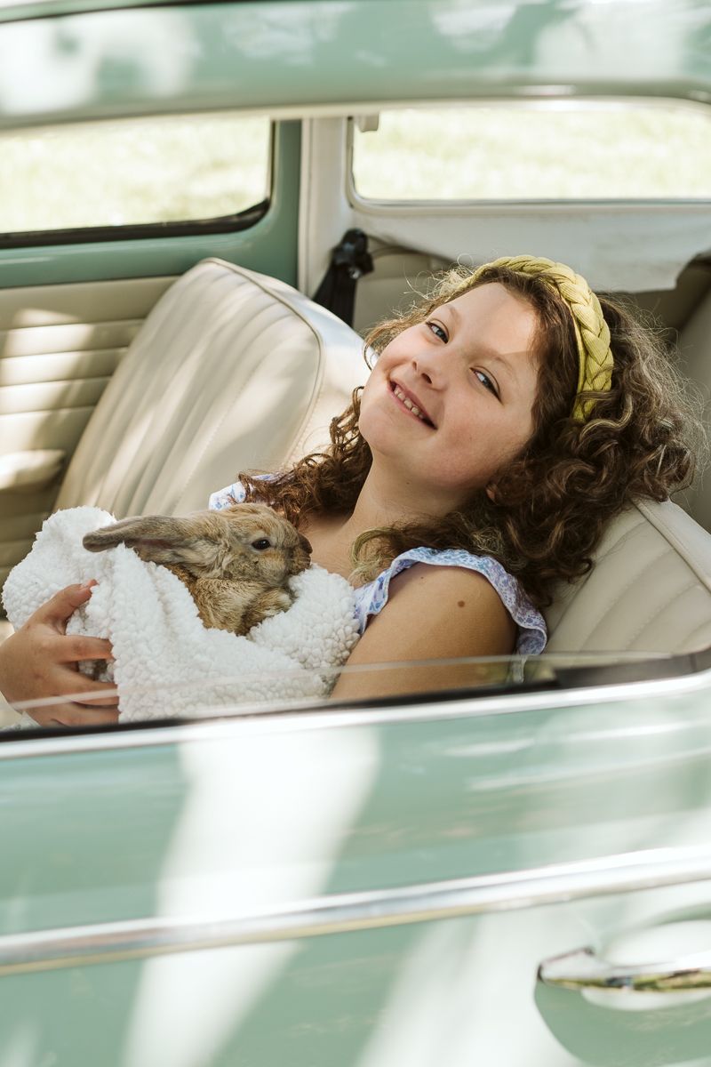 Person lying down and laughing joyfully in the backseat of a vintage mint green car.