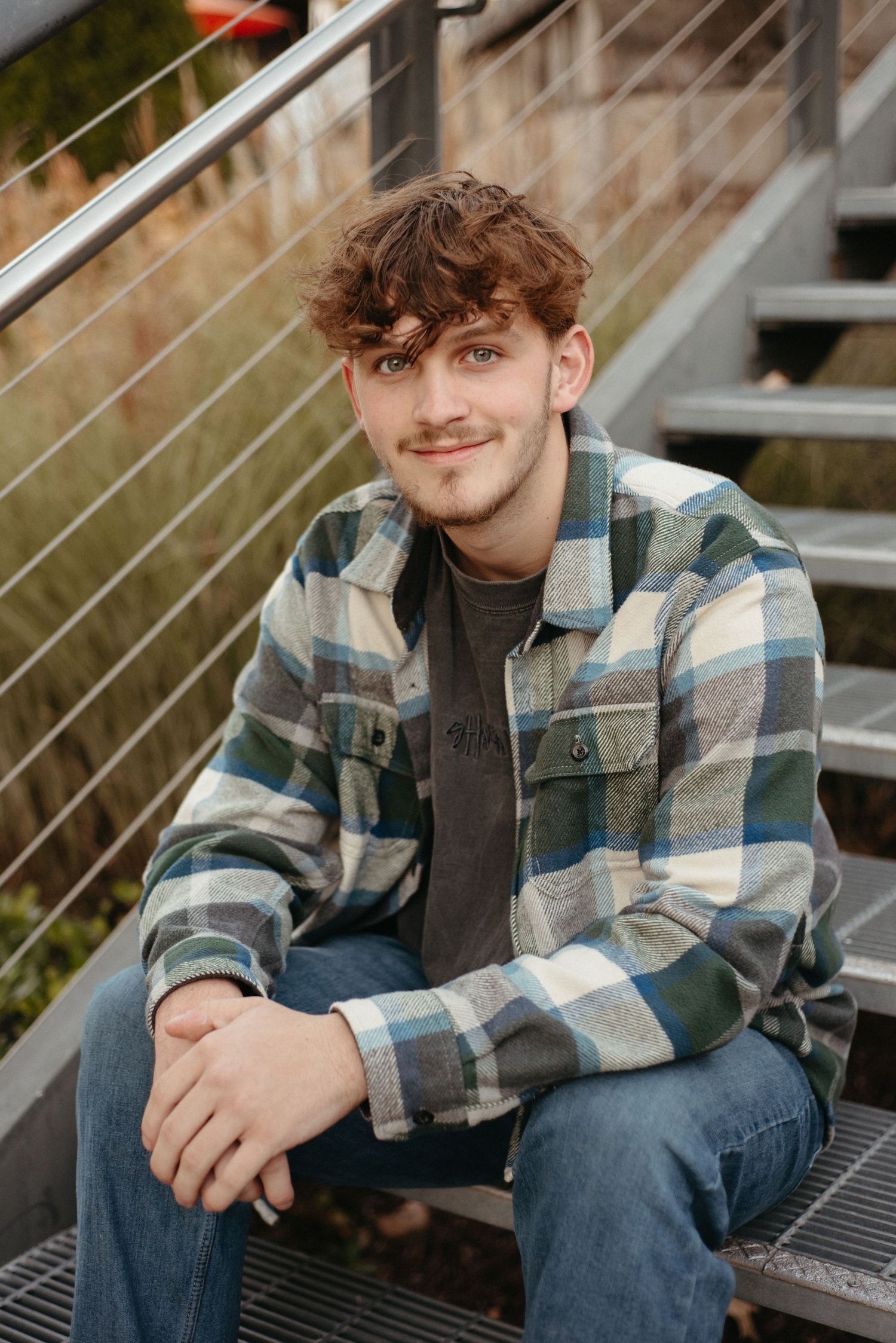 Casual portrait of someone sitting on steps wearing a plaid flannel jacket and jeans.