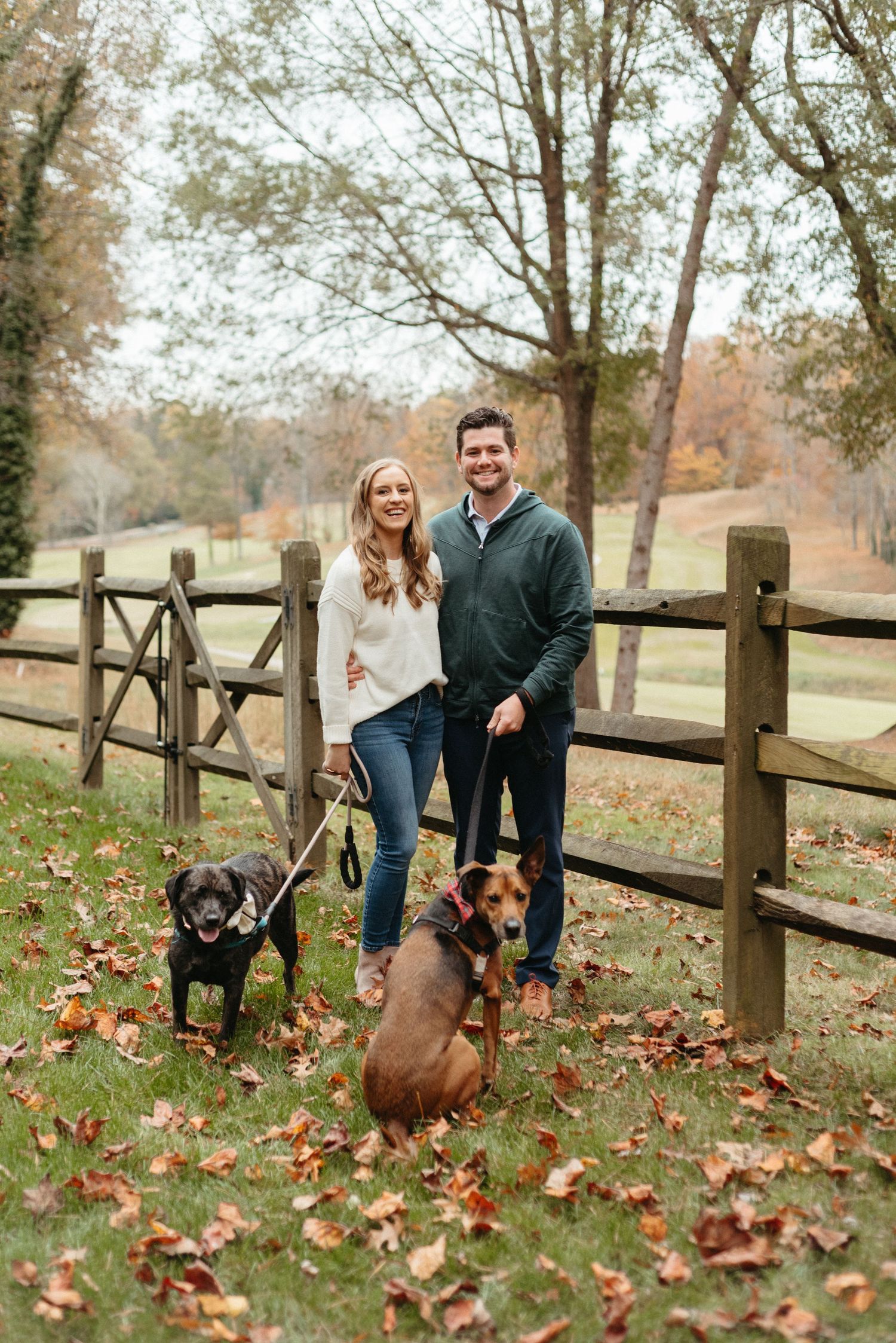 Autumn engagement photos with couple and their two dogs by rustic wooden fence.
