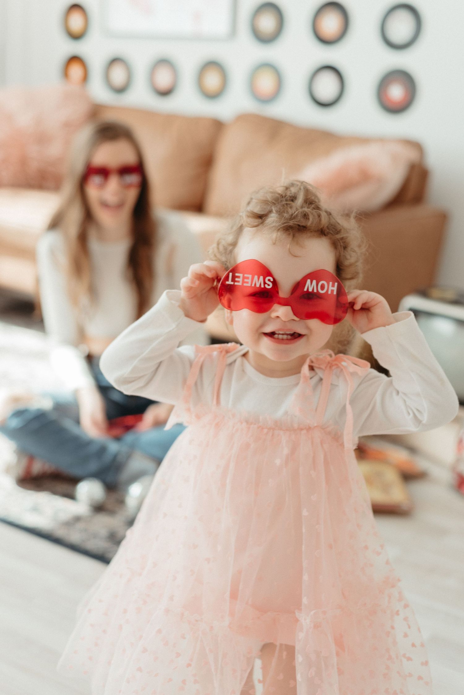 Someone wearing a pink tulle dress holds heart-shaped glasses in front of their face while posing for Valentine's Day photos.