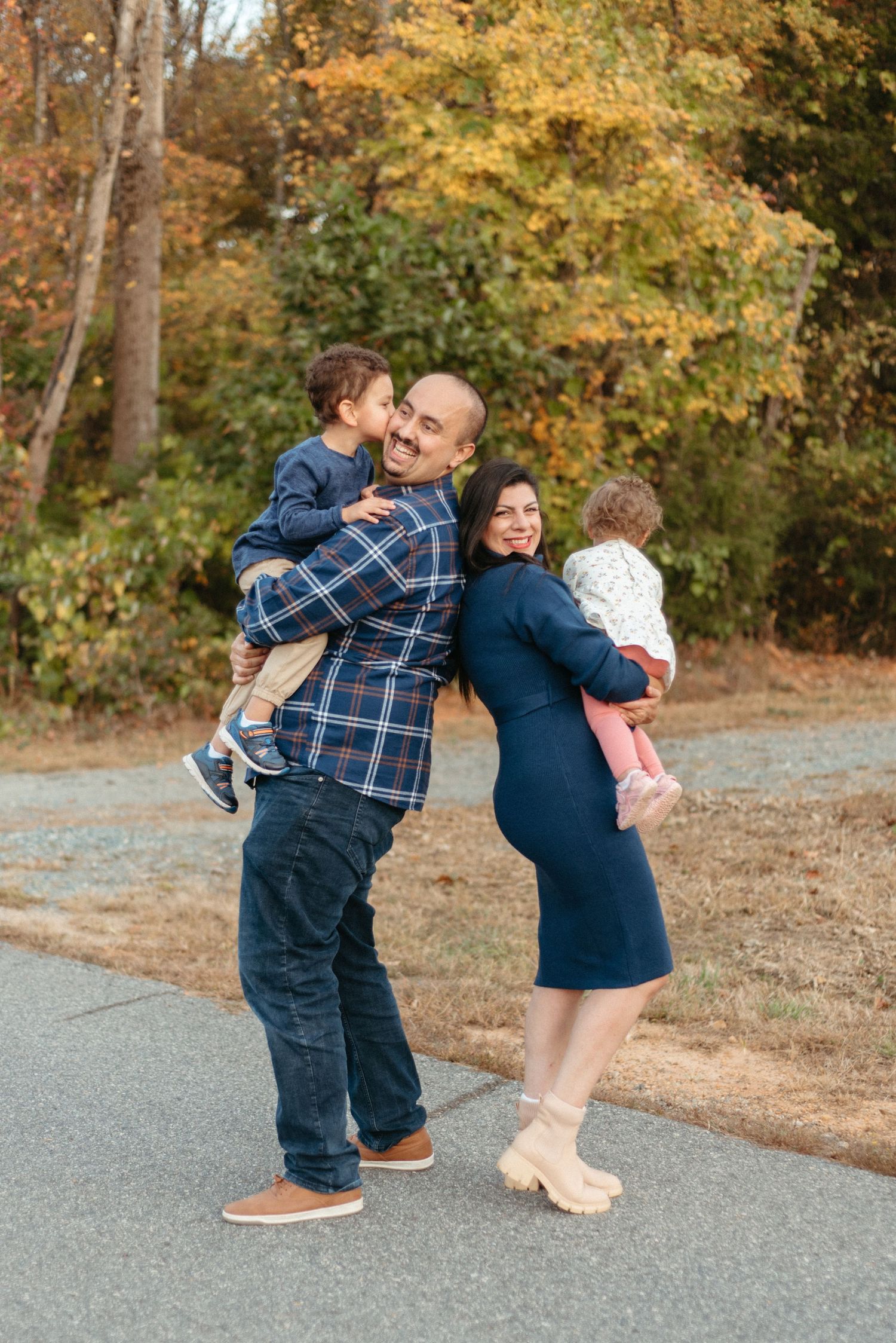 Playful family moment captured outdoors during autumn with fall foliage in background.
