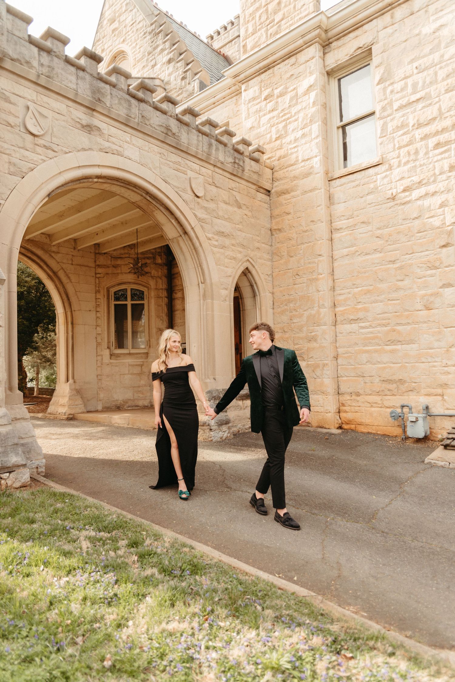 A couple walking together in formal wear outside a historic stone building.