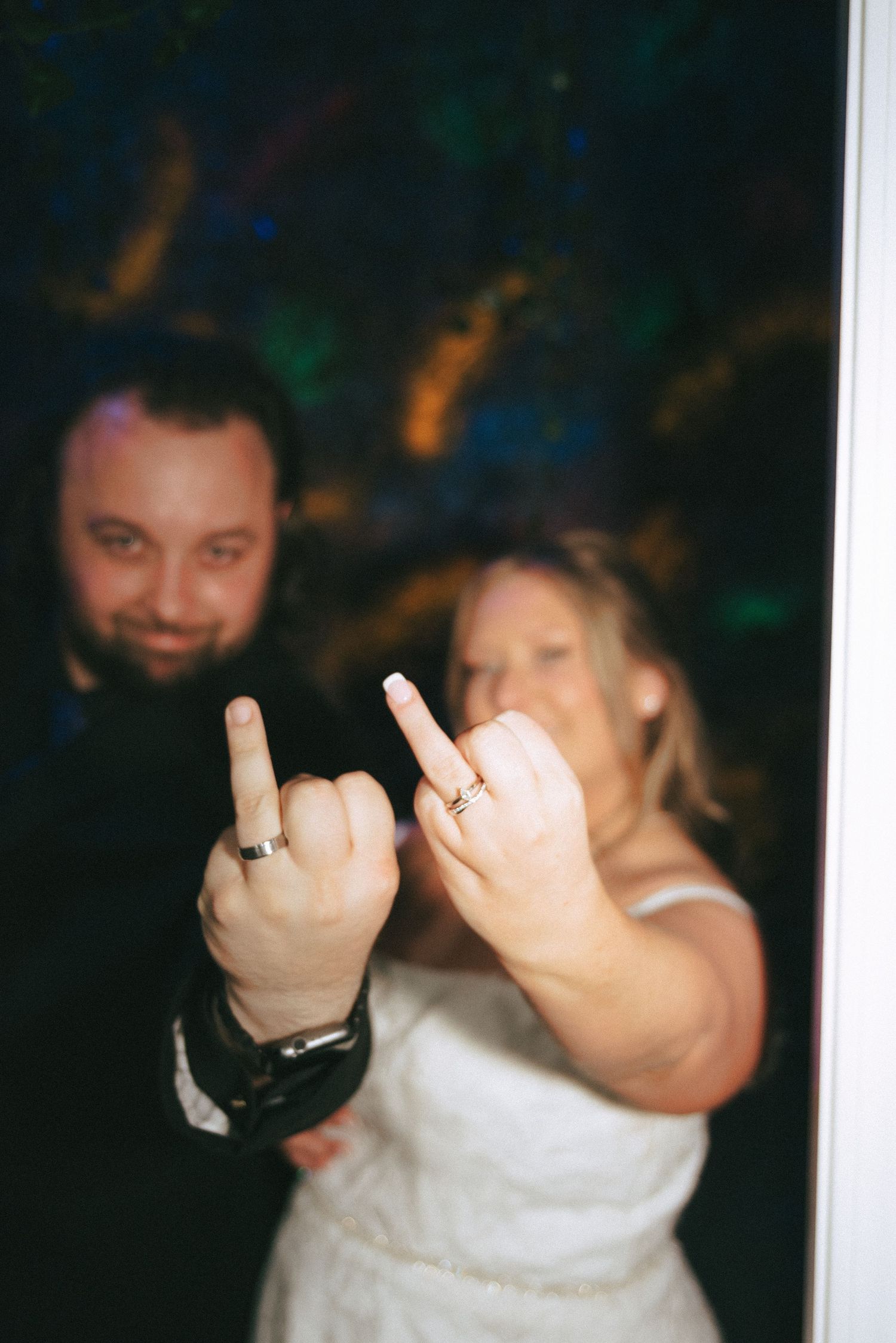 Close-up of wedding rings displayed on raised fingers in a dimly lit setting.