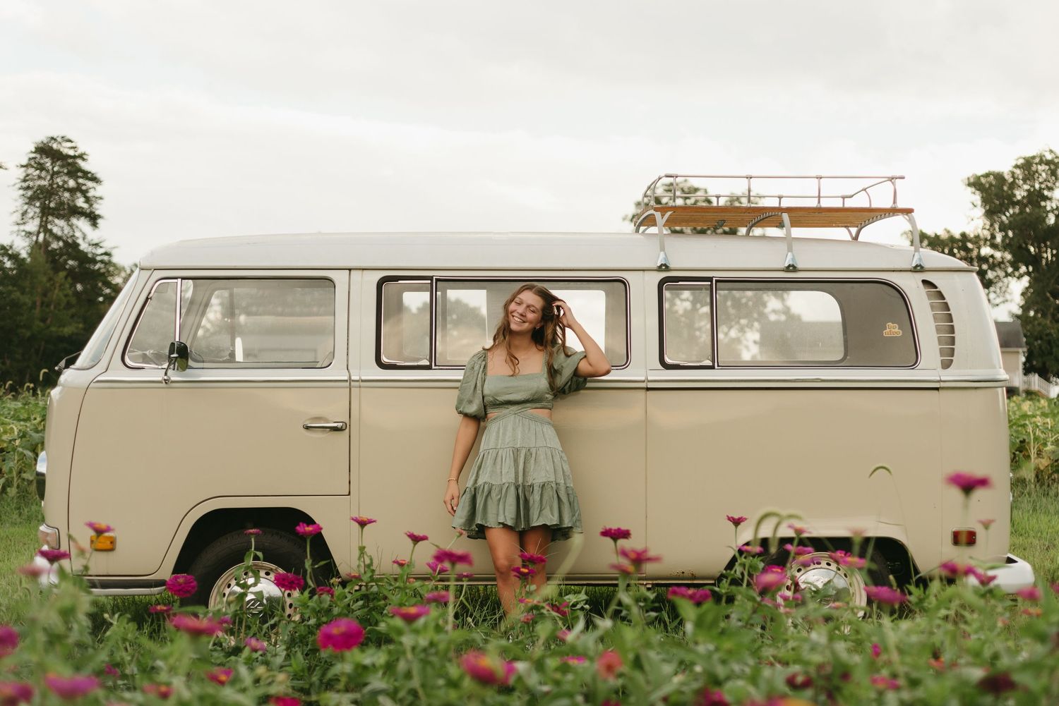 A vintage cream-colored Volkswagen van sits parked in a wildflower field.