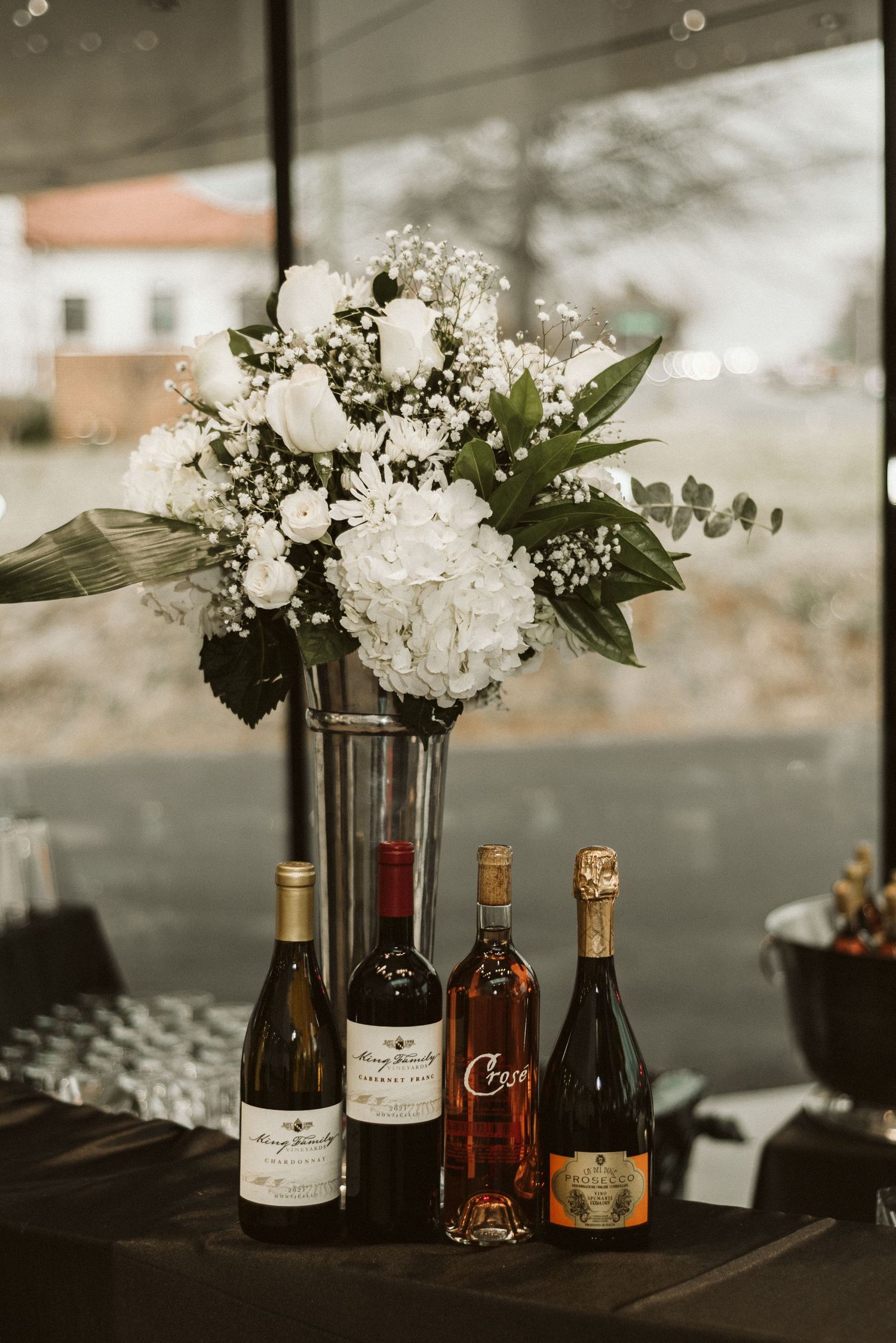 Elegant bar setup with wine bottles and white floral arrangements at an event.