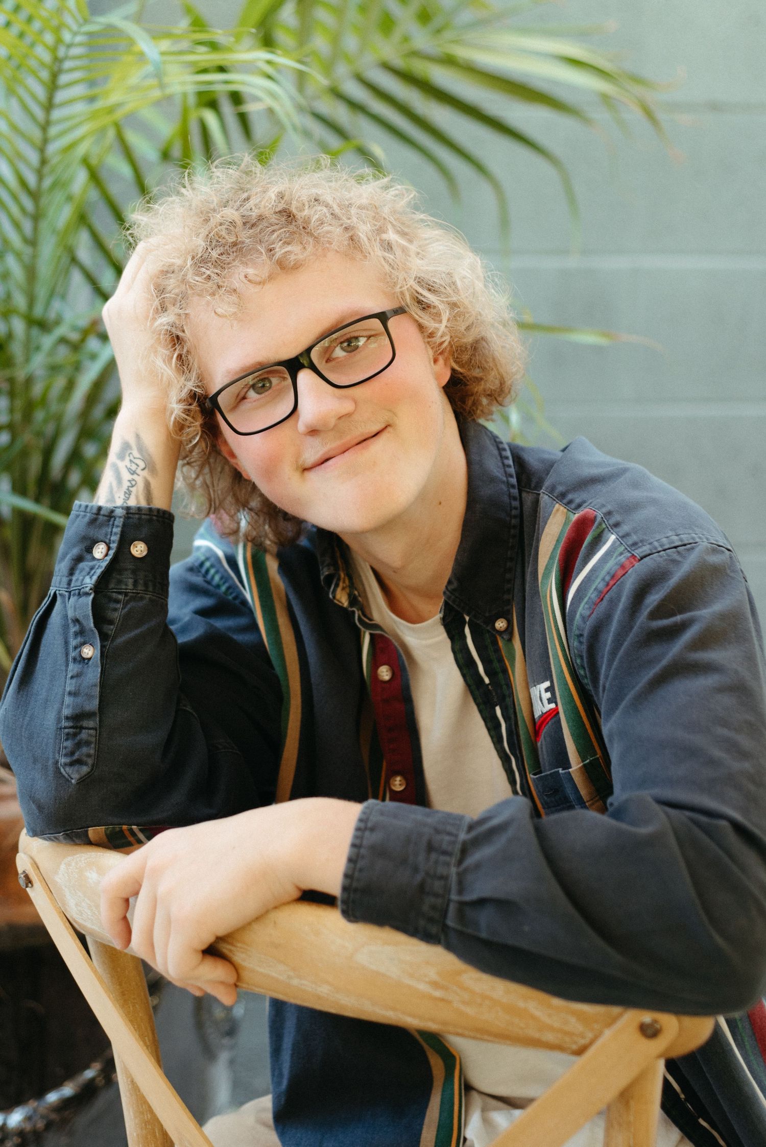 Casual portrait series leaning on wooden furniture with plants in background.