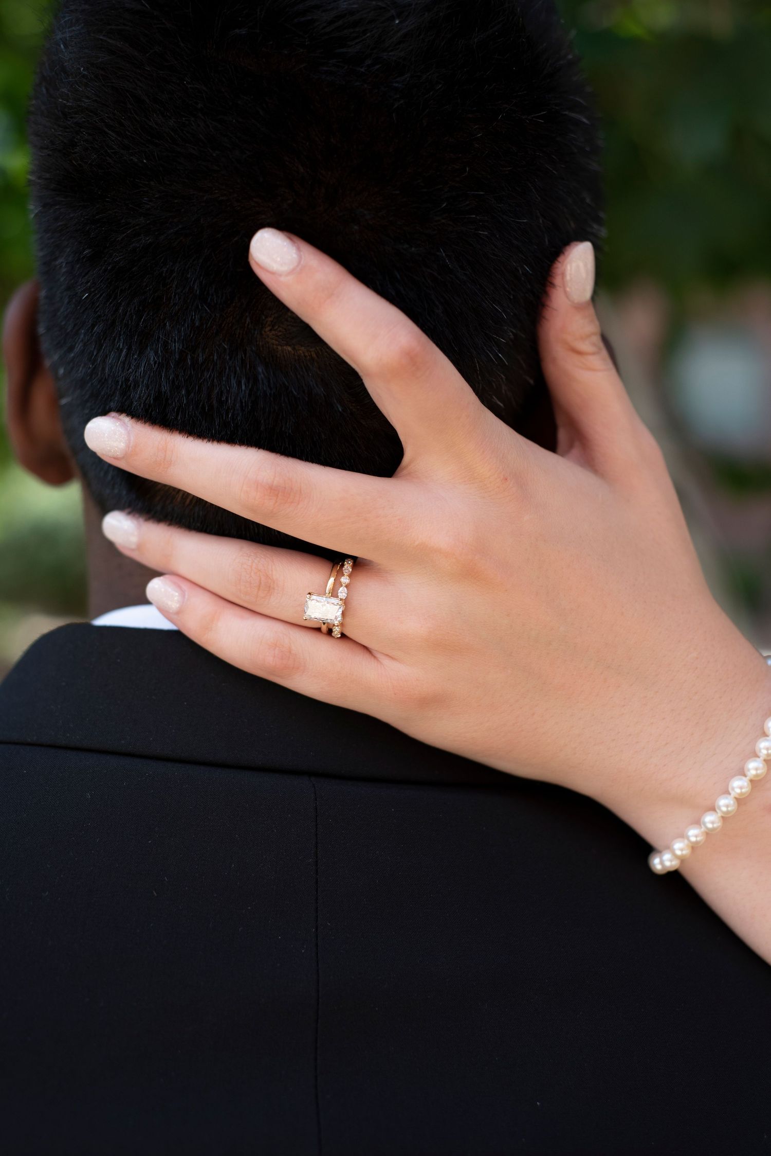 Close-up of a hand with engagement ring resting on a dark surface.