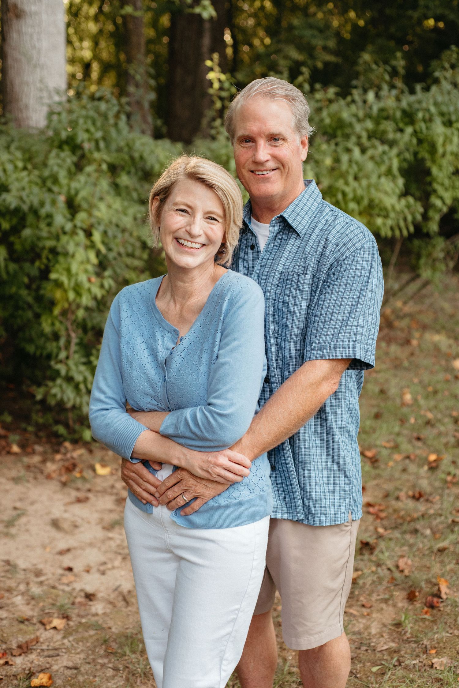 Mature couple embraces while posing for outdoor portrait in casual attire.