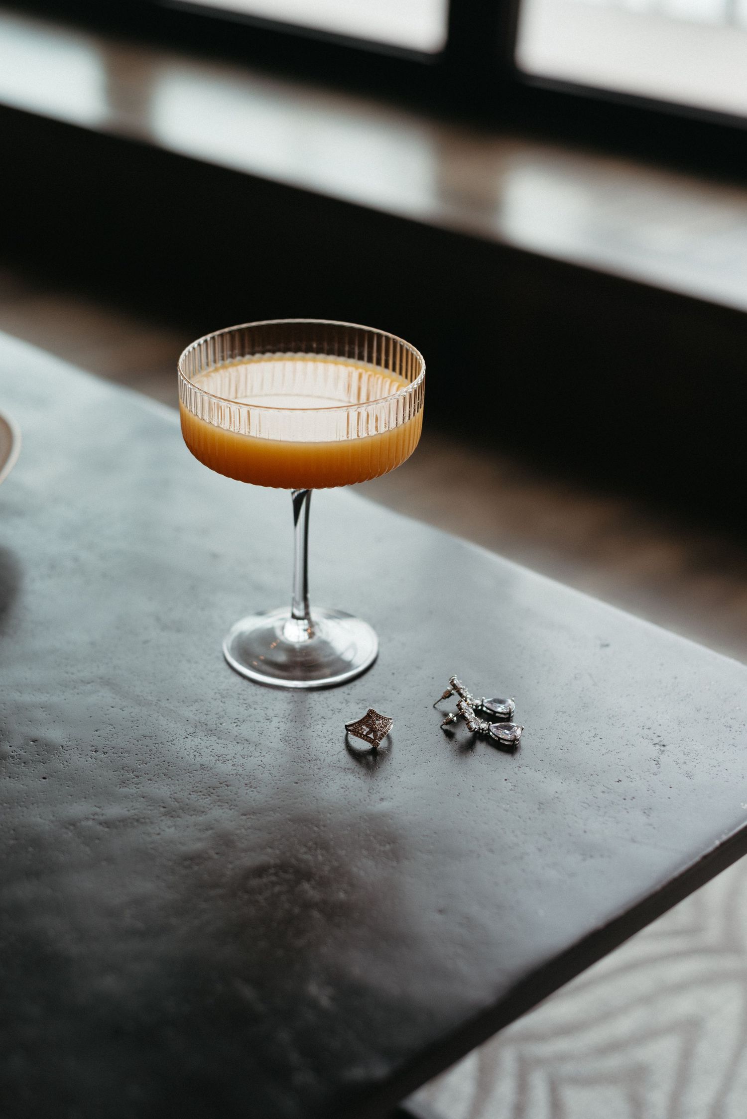 Craft cocktail in coupe glass on dark surface with dramatic lighting.