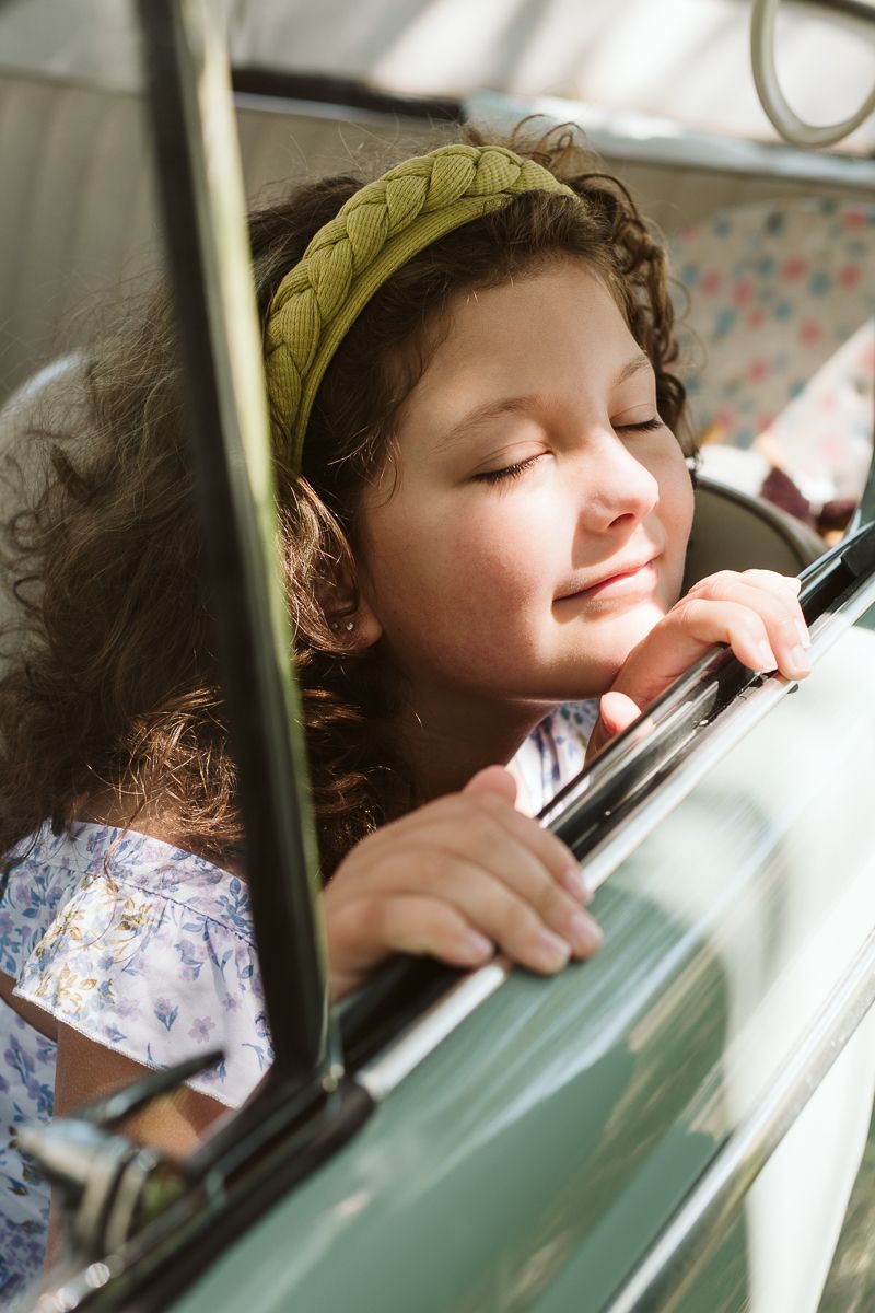 A child leans against a car window during a road trip, appearing to be peacefully asleep.