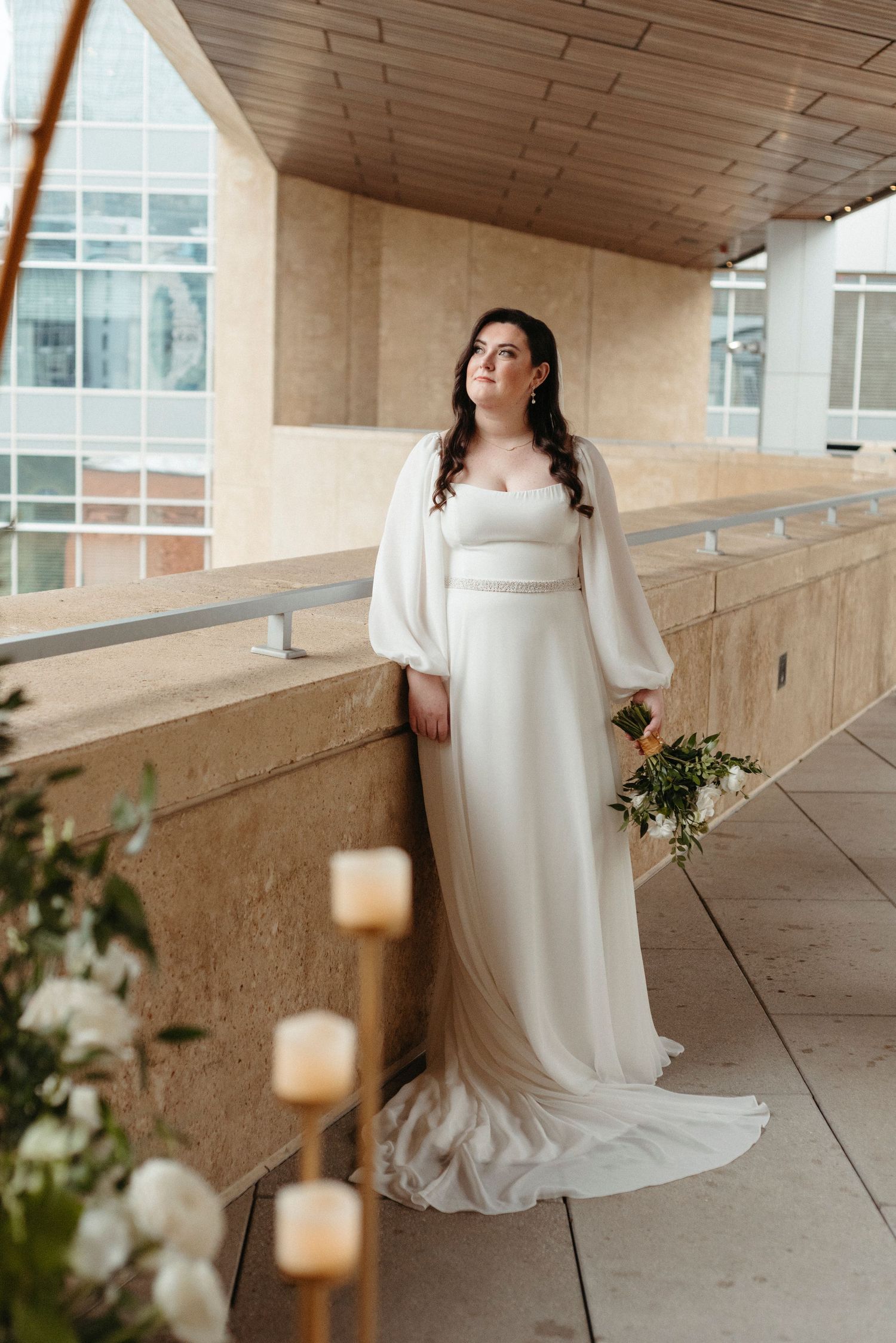 Bride in flowing white dress poses in modern architectural setting with dramatic lighting.
