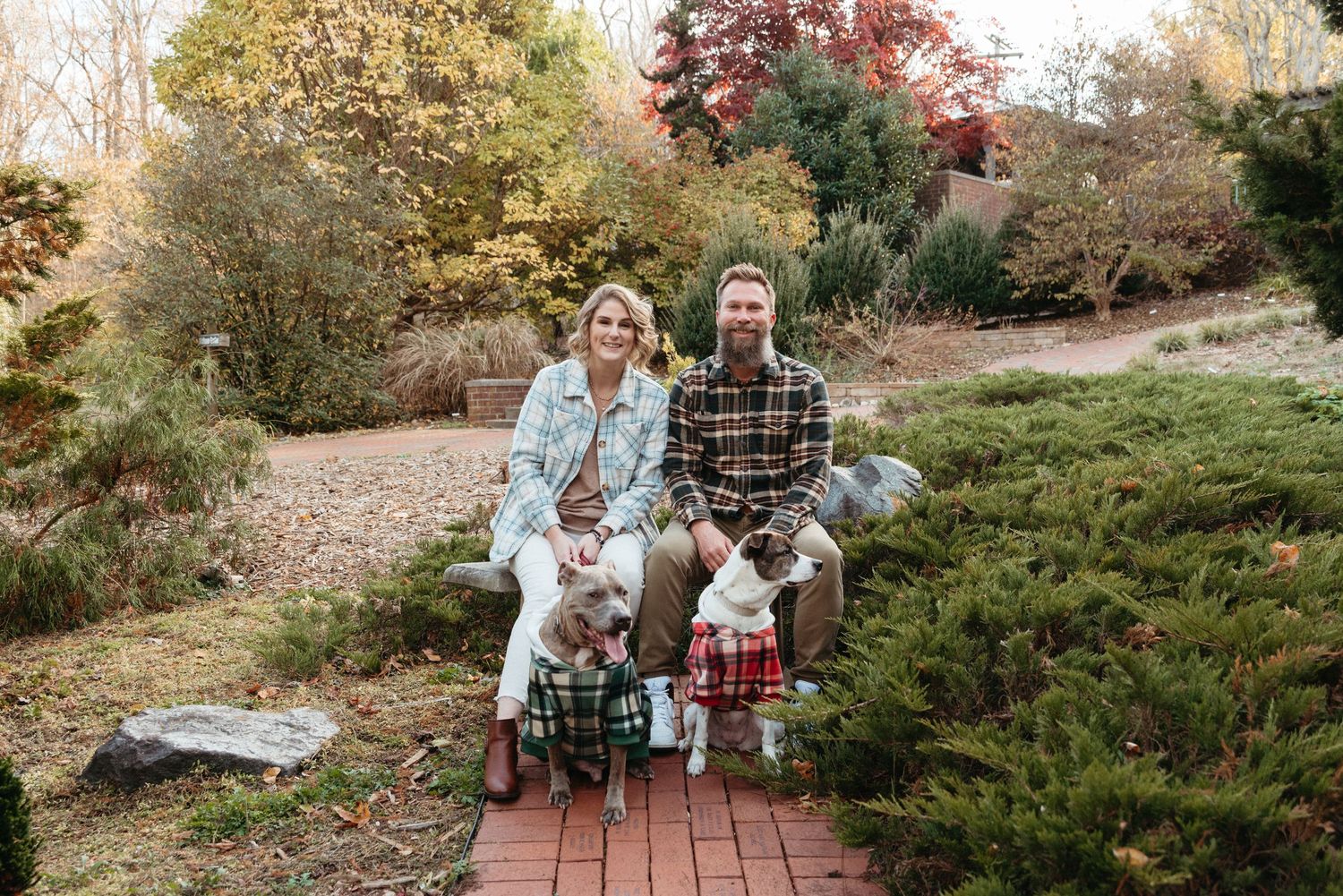A family in casual winter clothing sits together on brick steps surrounded by autumn foliage.