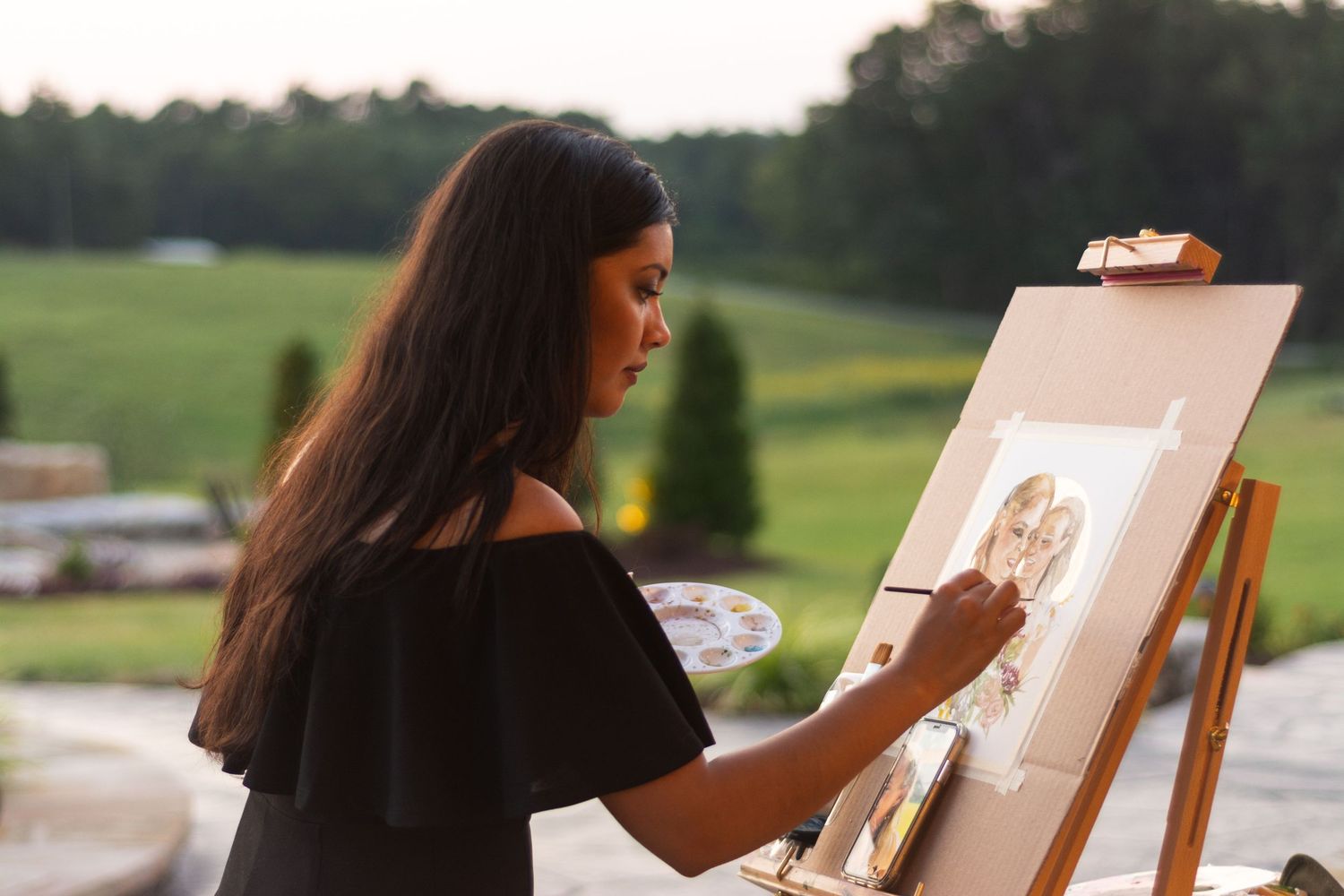 An artist works on a painting at an outdoor easel during a sunny day.