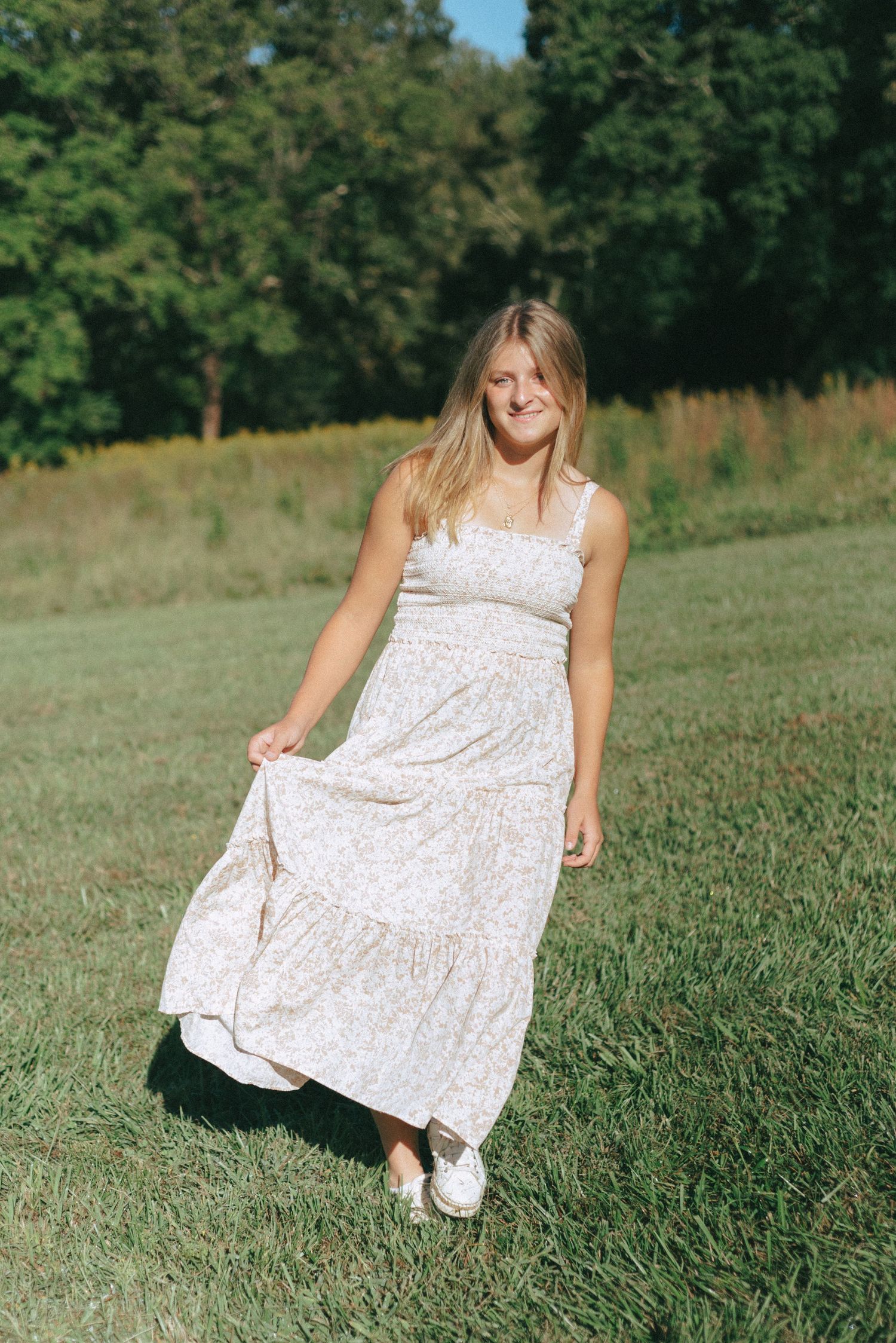 A white floral dress flows gracefully across a grassy meadow on a sunny summer day.