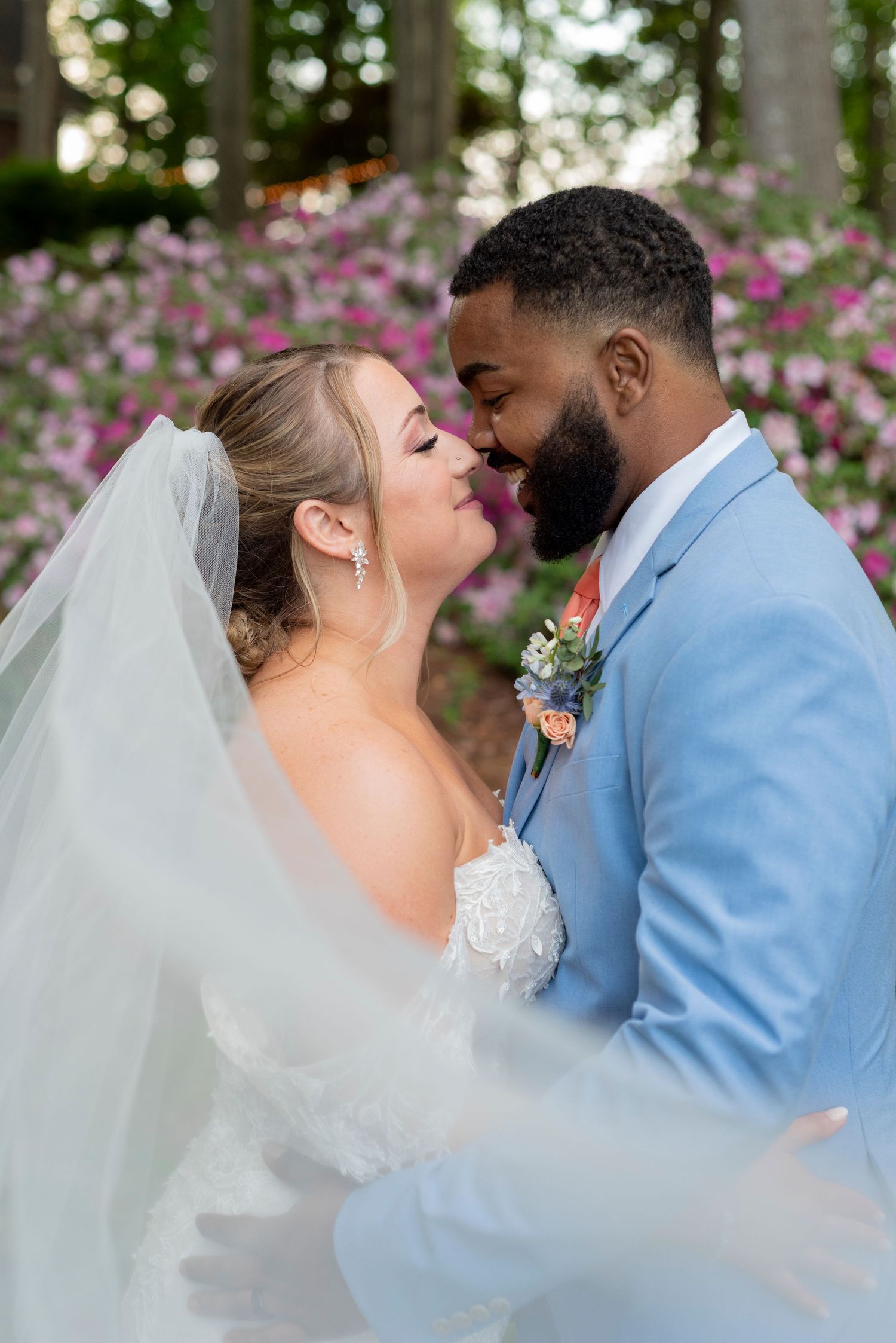A romantic wedding kiss sequence between a couple in a light blue suit and white dress against a floral backdrop