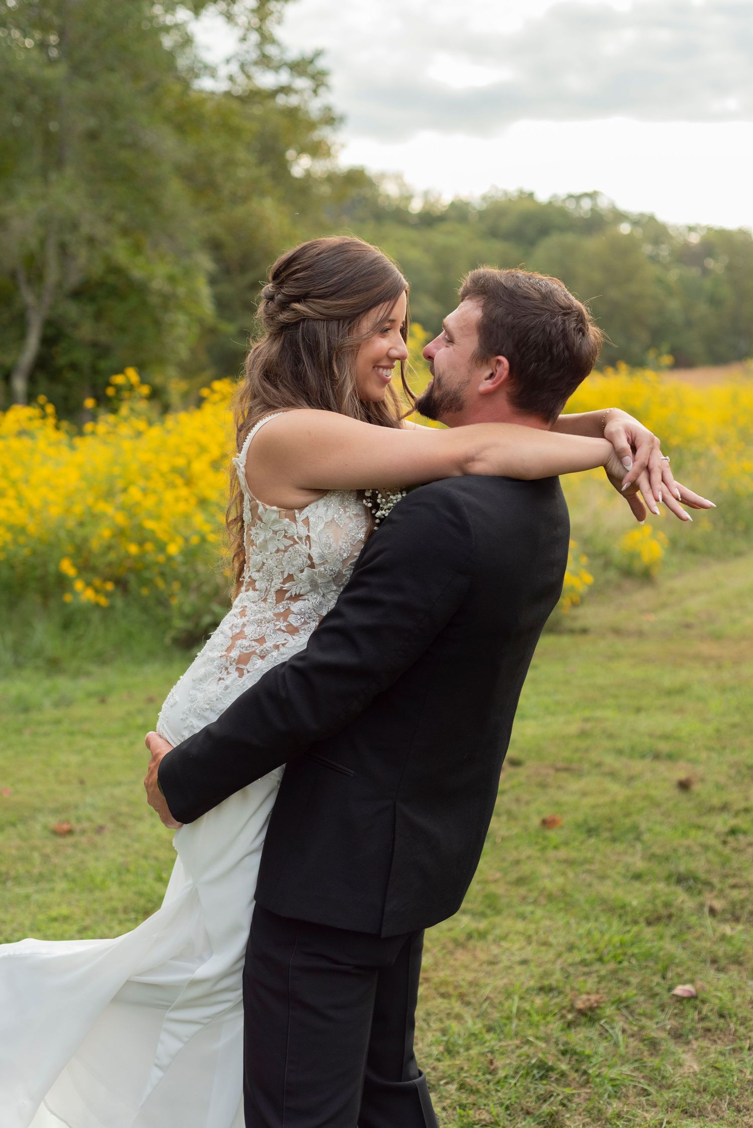 A couple in their wedding attire embrace in a field of yellow wildflowers during a romantic outdoor photo session after the ceremony.
