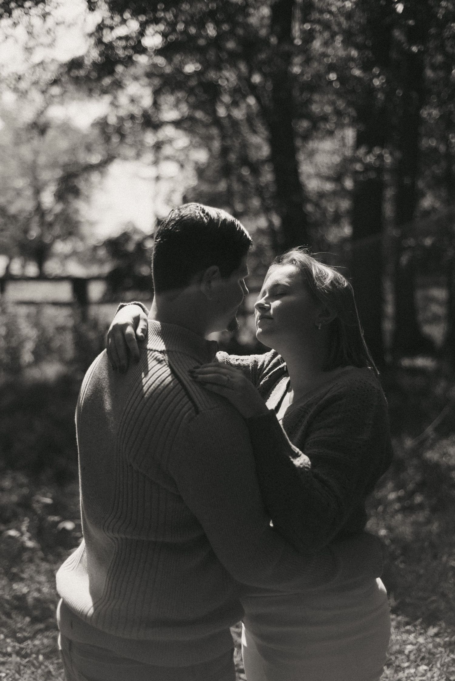 Black and white photo of a romantic couple embracing in a wooded outdoor setting.