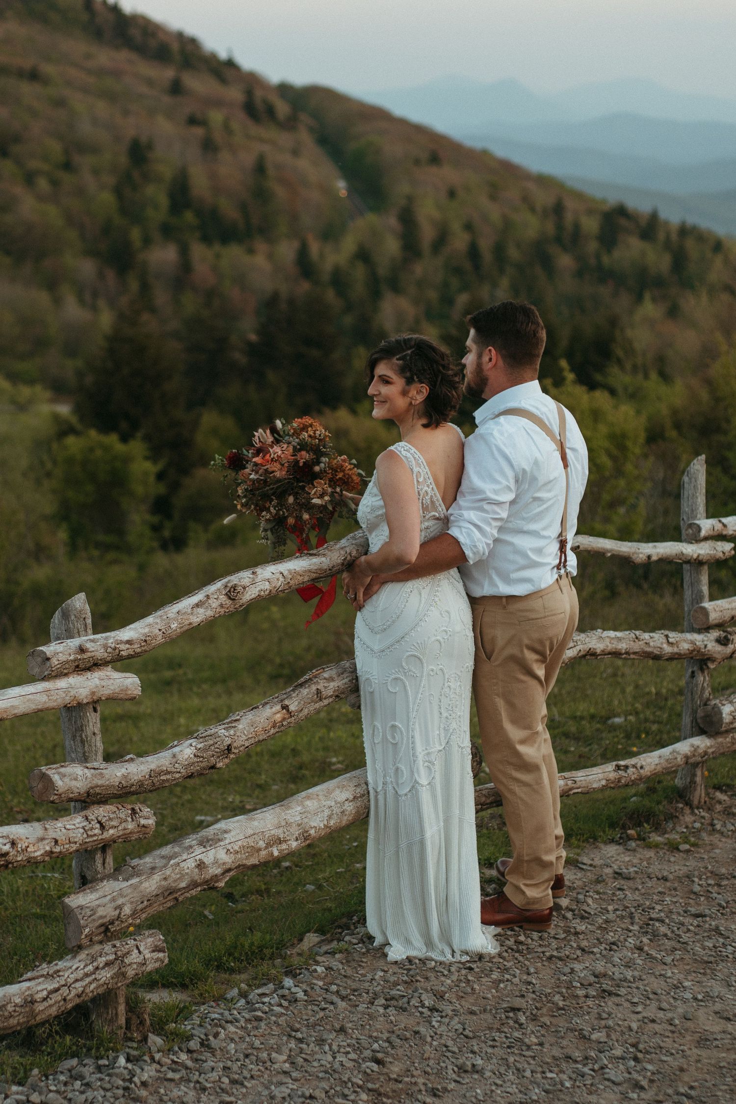 Couple shares romantic moment on mountaintop overlooking misty mountain ranges.