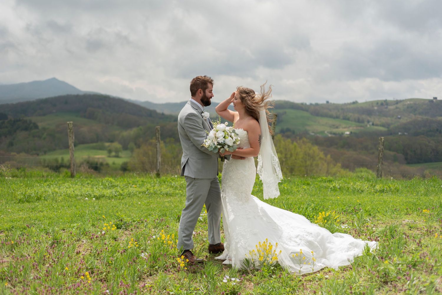 Couple in wedding attire embraces on a scenic hillside meadow with rolling mountains in the background.