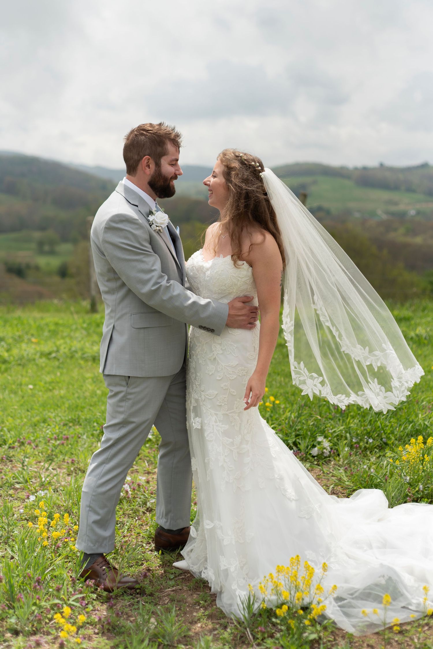 Newlyweds share an intimate moment in a field of wildflowers with mountains visible in the distance.