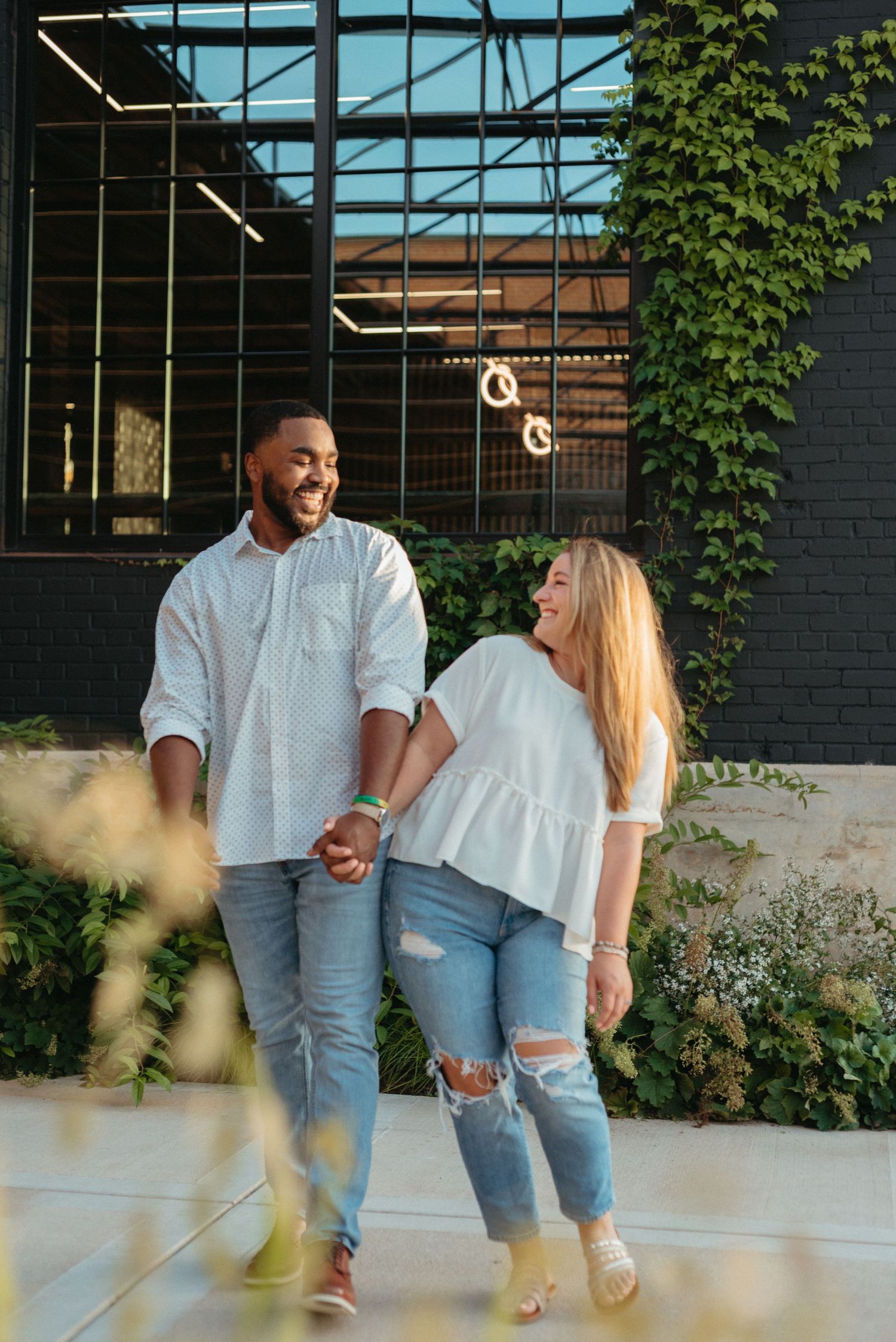 Couple in matching white tops and ripped jeans holding hands while walking together outdoors.