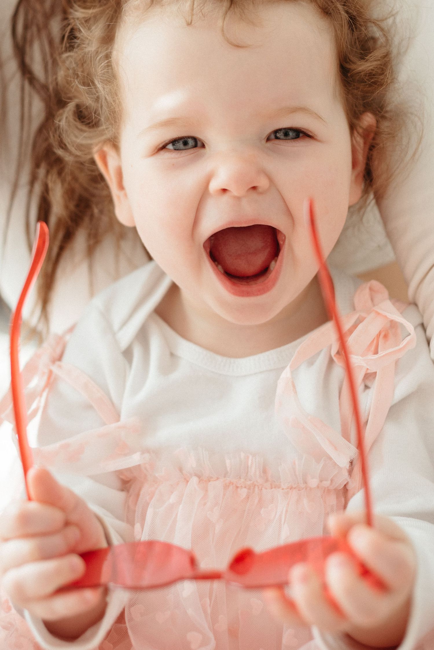 Joyful expression wearing a white and pink outfit while holding red ribbons or streamers in both hands.