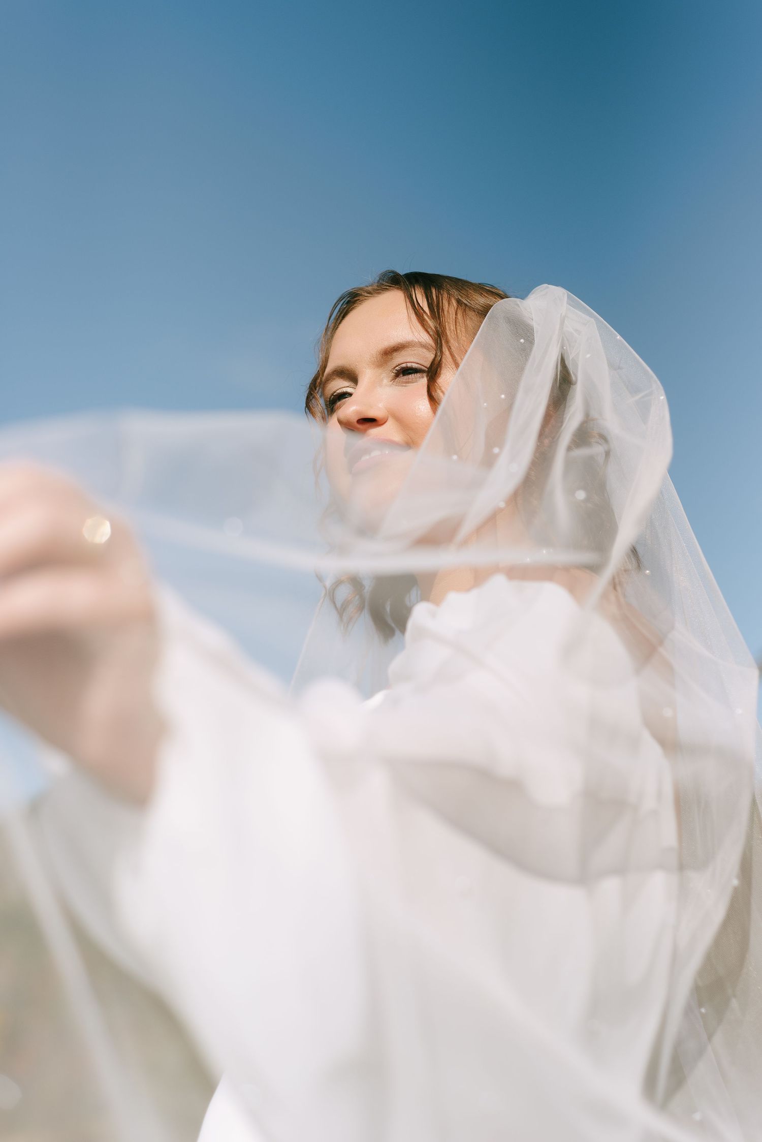 Ethereal white veil flowing in the breeze against a bright blue sky.