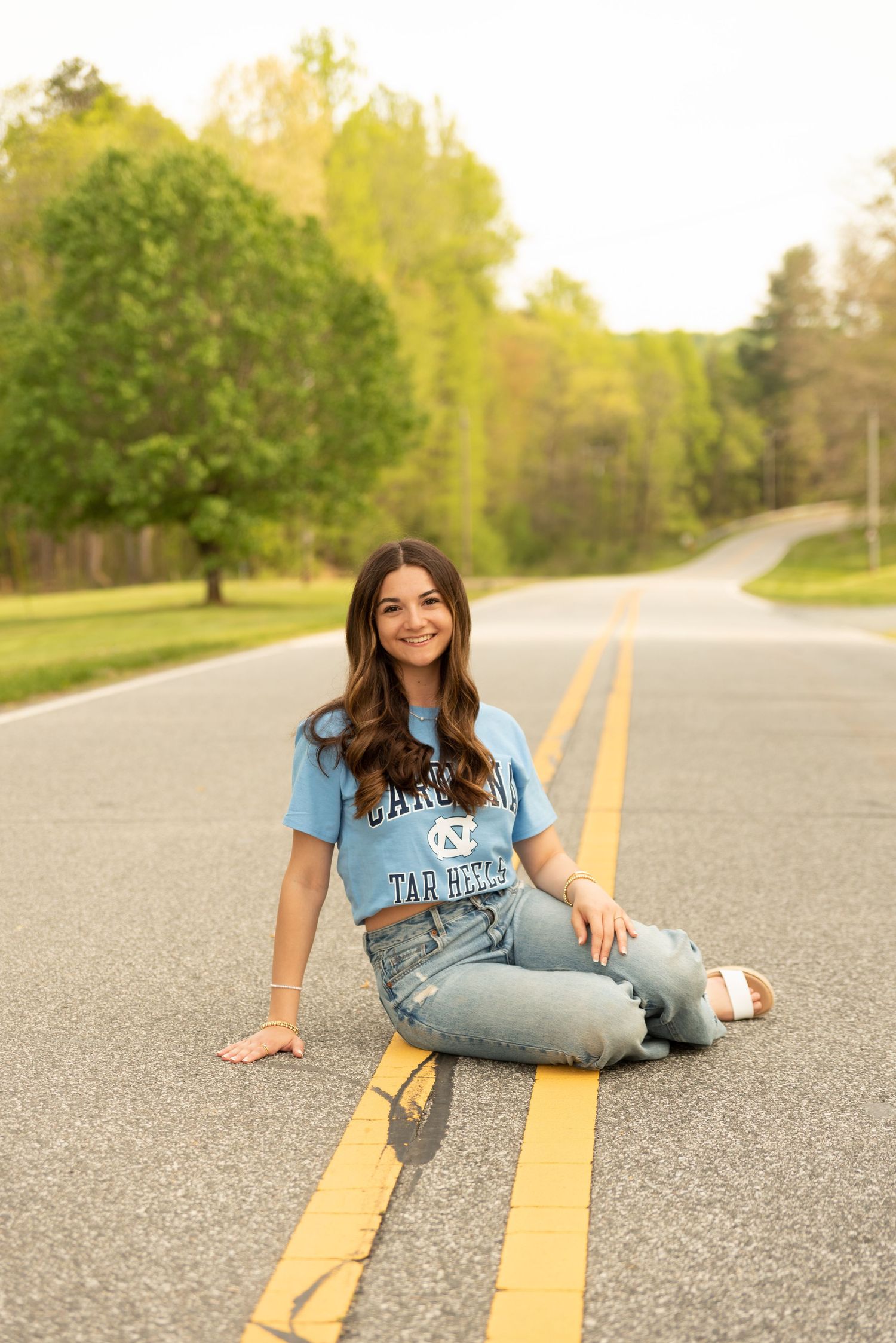 Person in light blue t-shirt and jeans sitting playfully on yellow road lines.