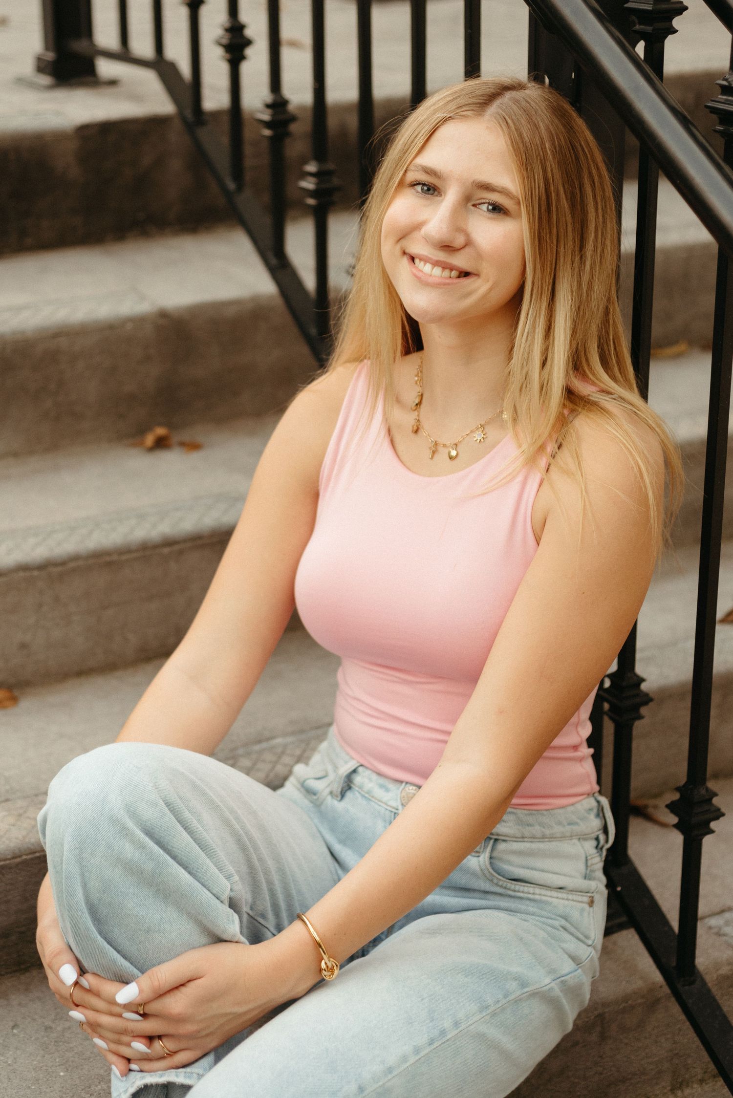 Person in pink tank top and light jeans sitting casually on outdoor steps.