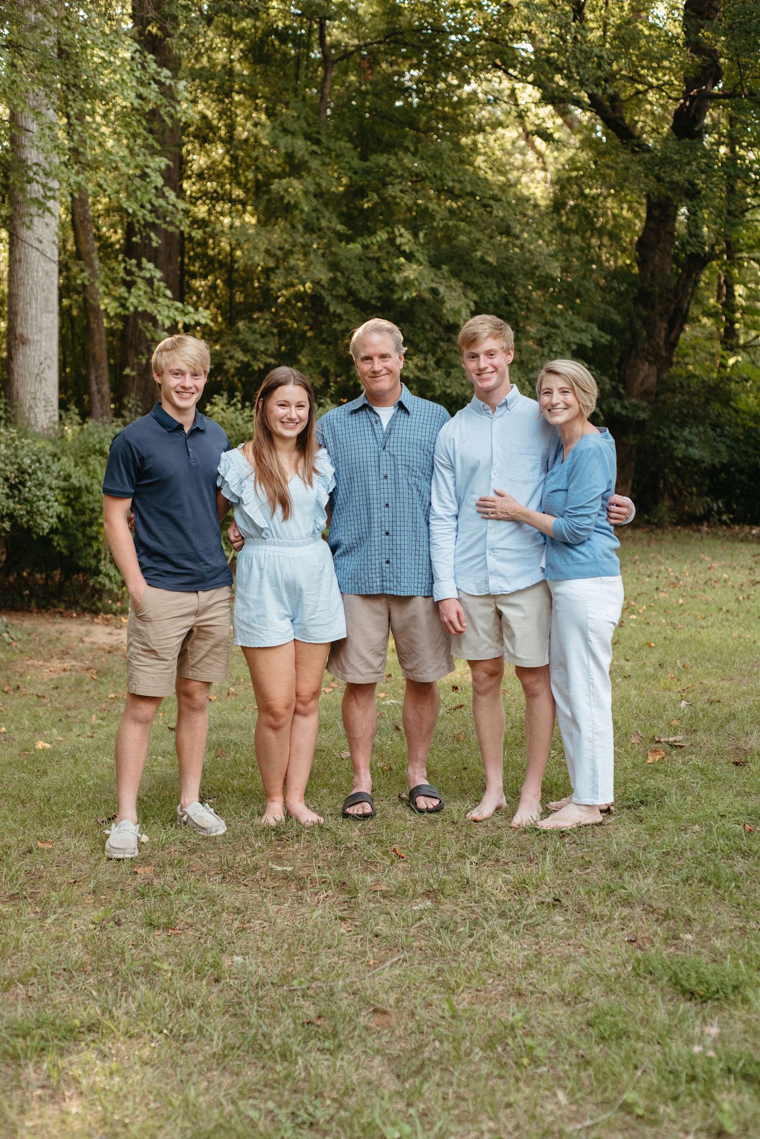 A family group wearing coordinated light blue and khaki outfits poses together outdoors in a natural setting.