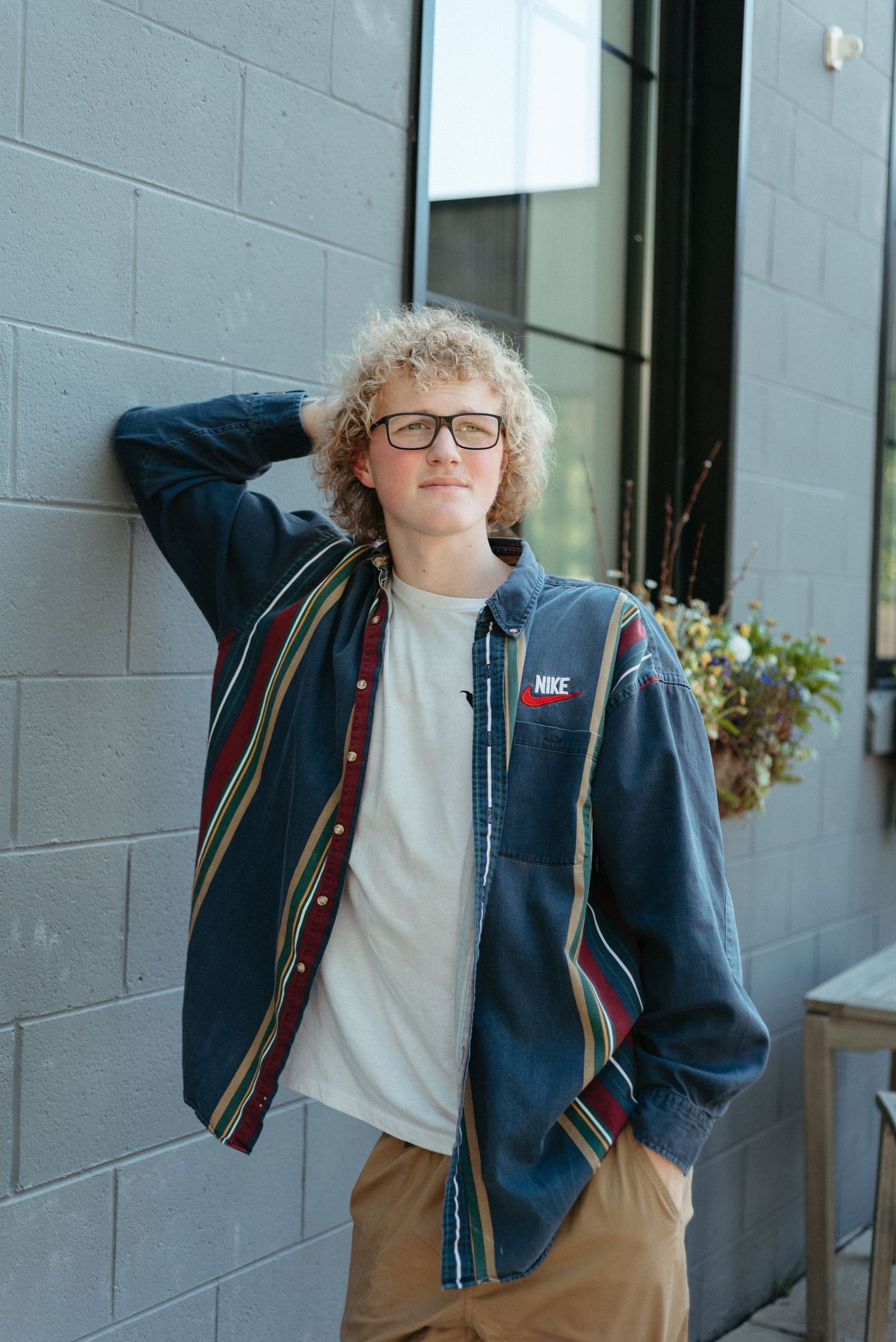 Playful poses against grey wall wearing blue jacket and backpack.