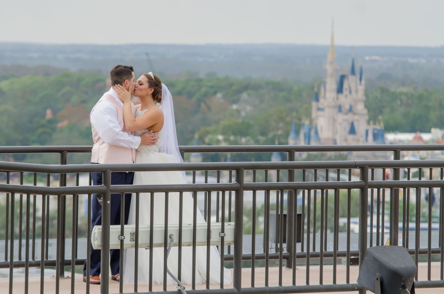 Newlyweds share a romantic kiss on a balcony overlooking Cinderella Castle at Walt Disney World on their wedding day.