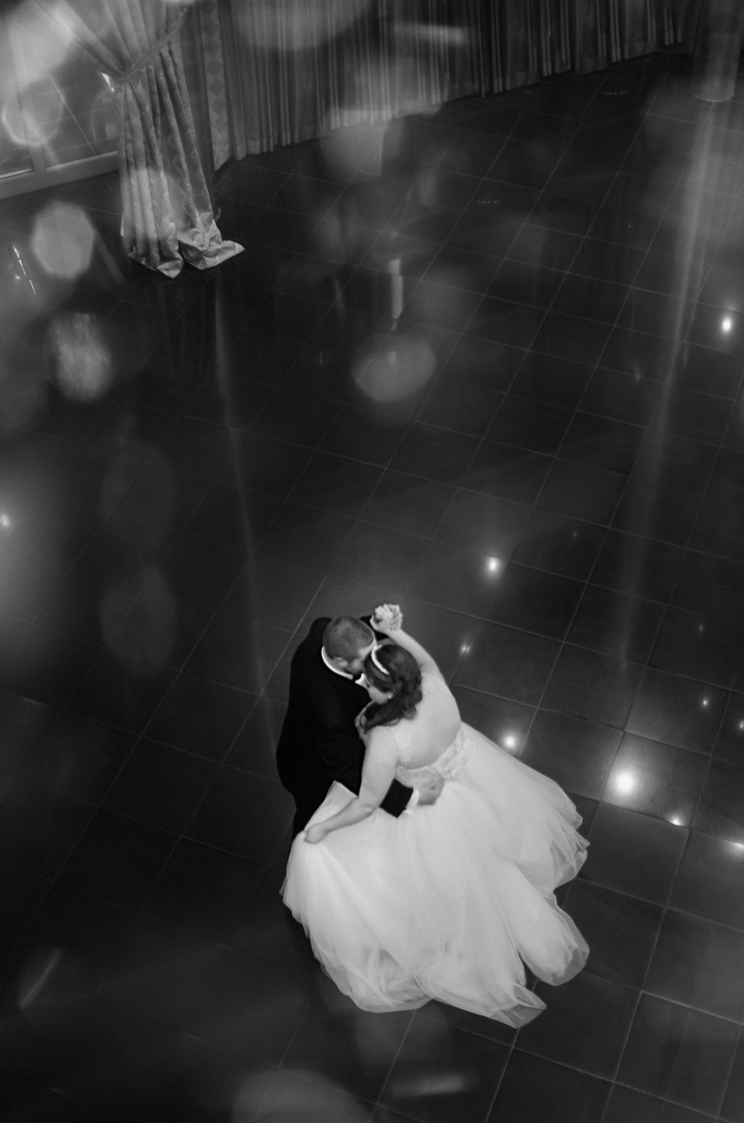 Aerial black and white photo of bride and groom sharing their first dance on a sparkling ballroom floor.