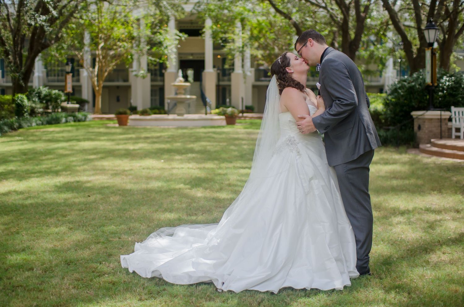 Bride and groom sharing a romantic kiss in a lush garden, with the bride in a flowing white gown and long veil.