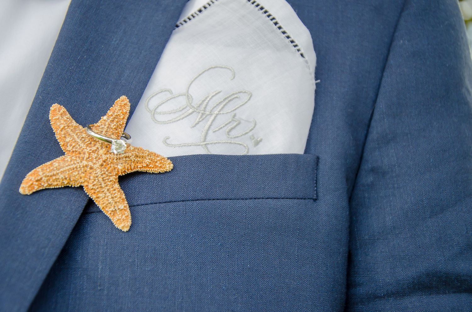 Blue suit jacket with starfish boutonniere and embroidered Mr. pocket square for a beach wedding.