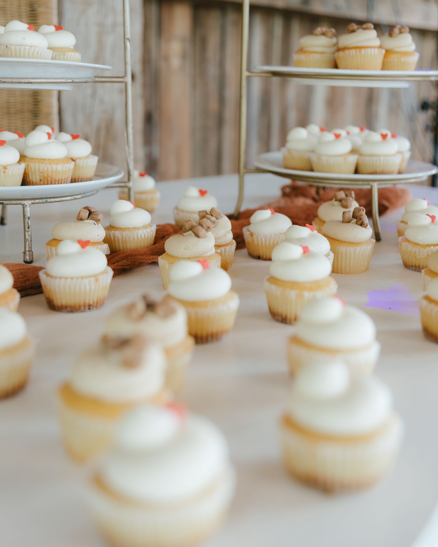 White frosted cupcakes with decorative toppers displayed on tiered stands and table at a wedding dessert bar.