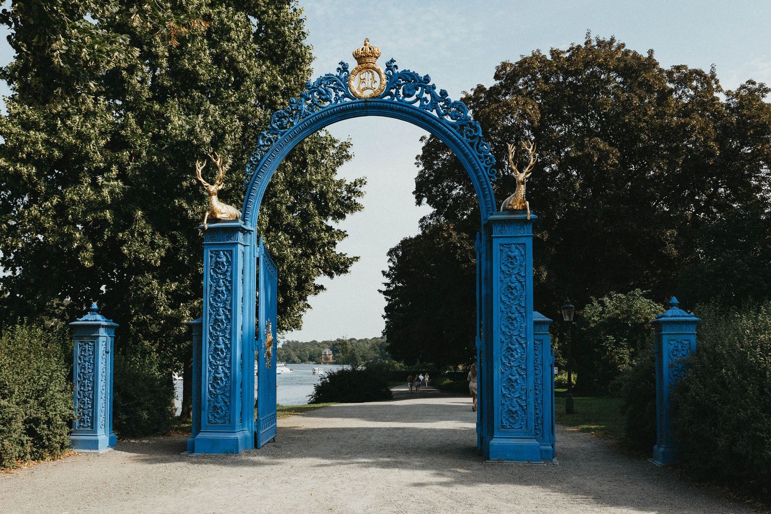 Ornate blue decorative iron arch gate with gold accents overlooking a serene lake.