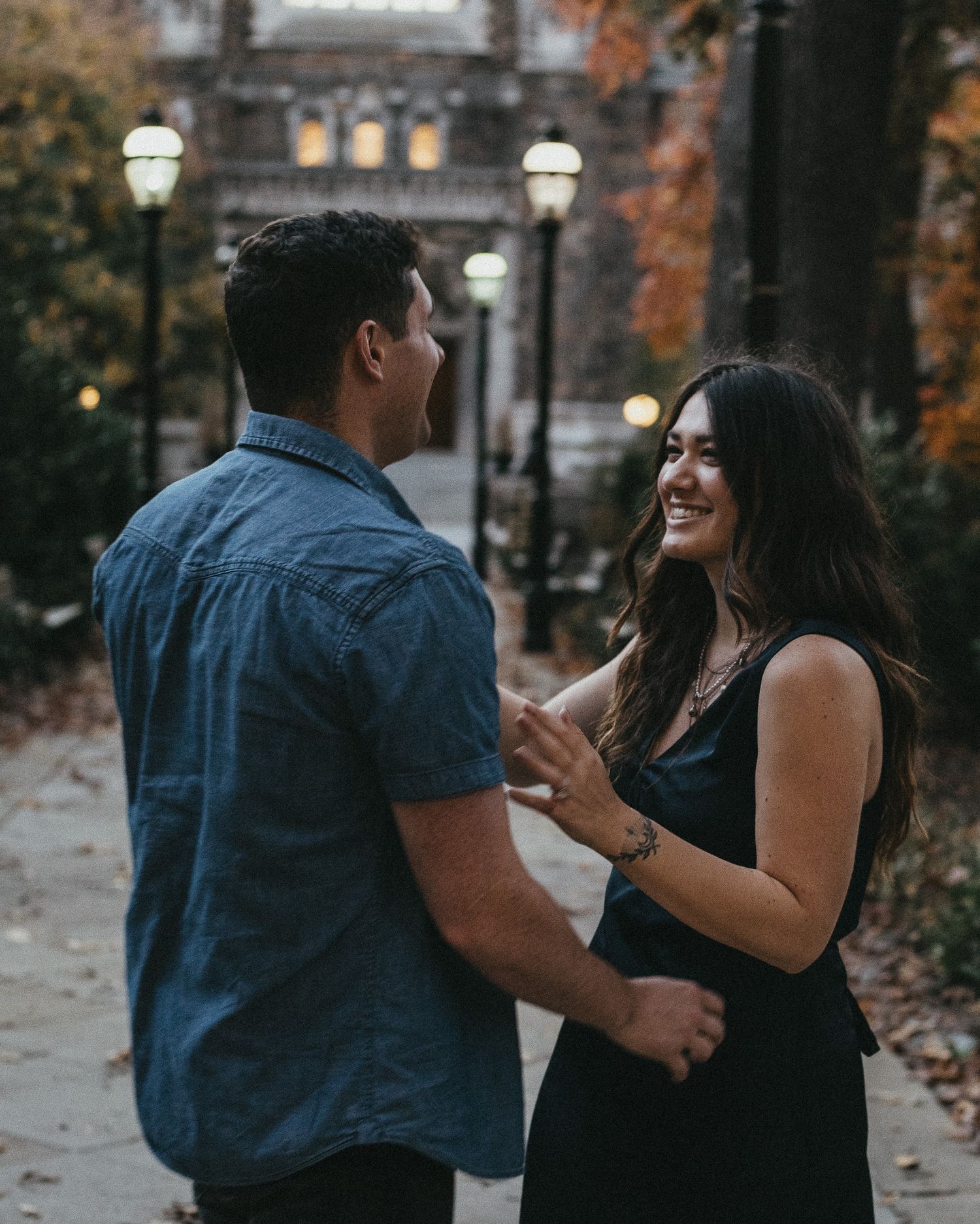A couple laughing during an evening engagement session at a historic Lehigh Valley university campus with glowing lampposts.