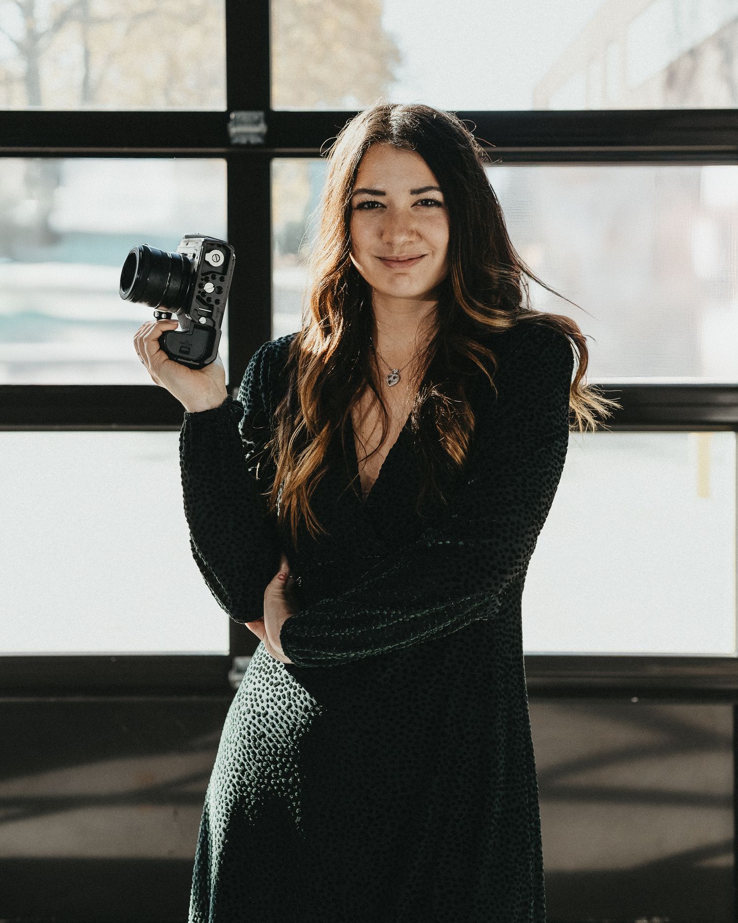 Professional wedding photographer in Northeast PA holding a camera, standing in front of a large window in a modern studio.