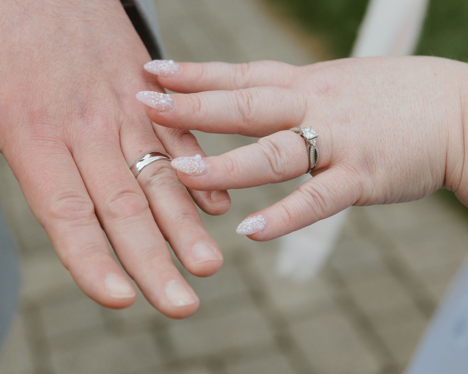 Close-up of a couple's hands showing matching silver wedding rings, with the bride wearing a diamond engagement ring.